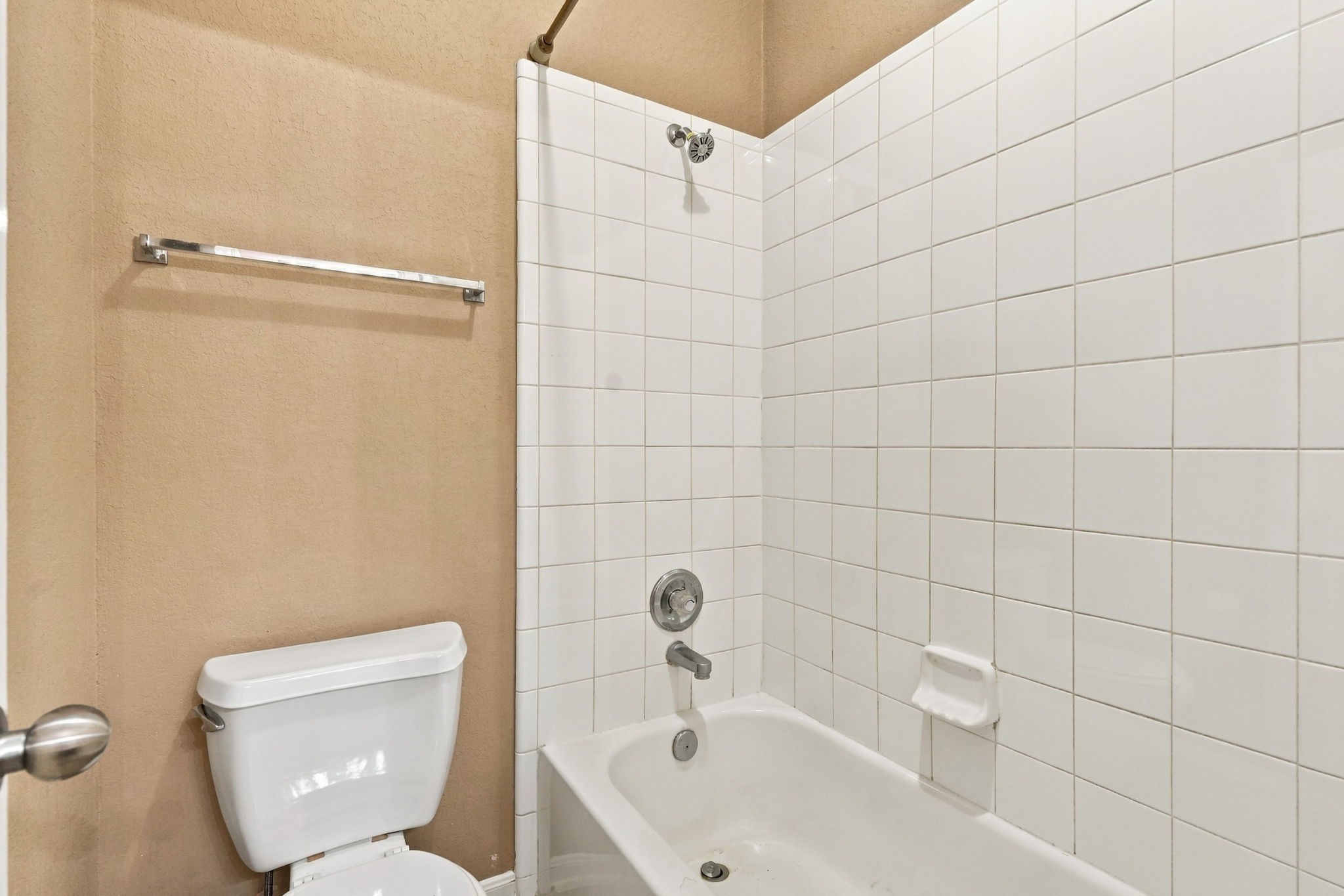A functional full bathroom featuring a tub-and-shower combination with white tile surround, and chrome fixtures.