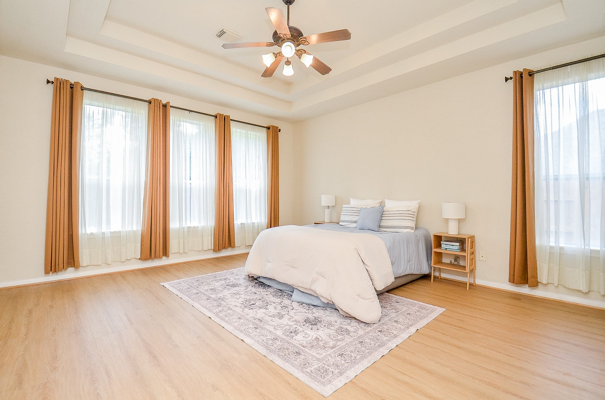 A primary suite with room to truly spread out. The tray ceiling adds architectural interest while multiple windows bring in natural light, and the generous proportions leave plenty of space beyond the bed for additional furniture or a sitting area.