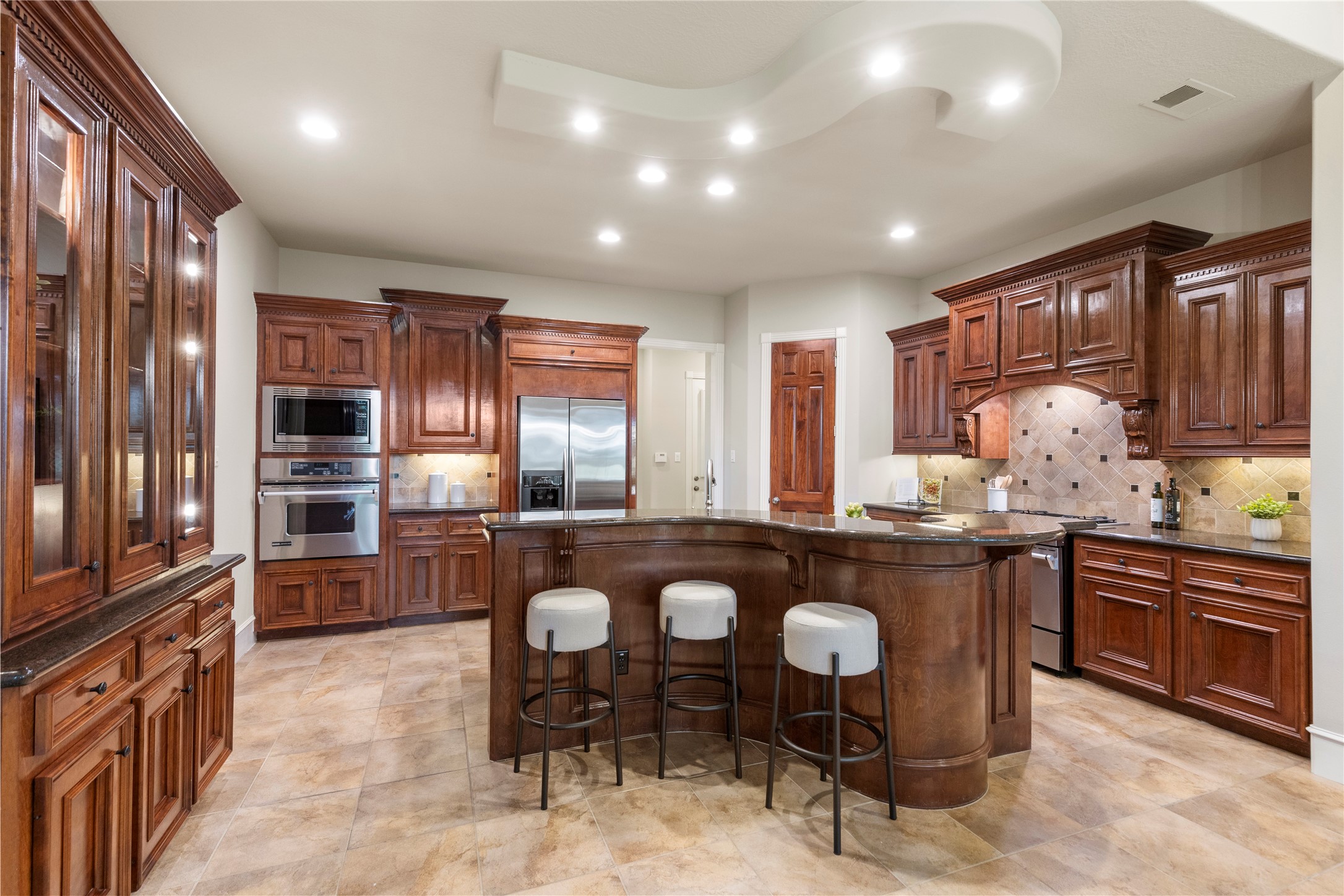 The kitchen offers a generous island, rich cabinetry, and an open connection to the breakfast area and den. The original custom design includes a distinctive piano shaped island, adding personality and function.