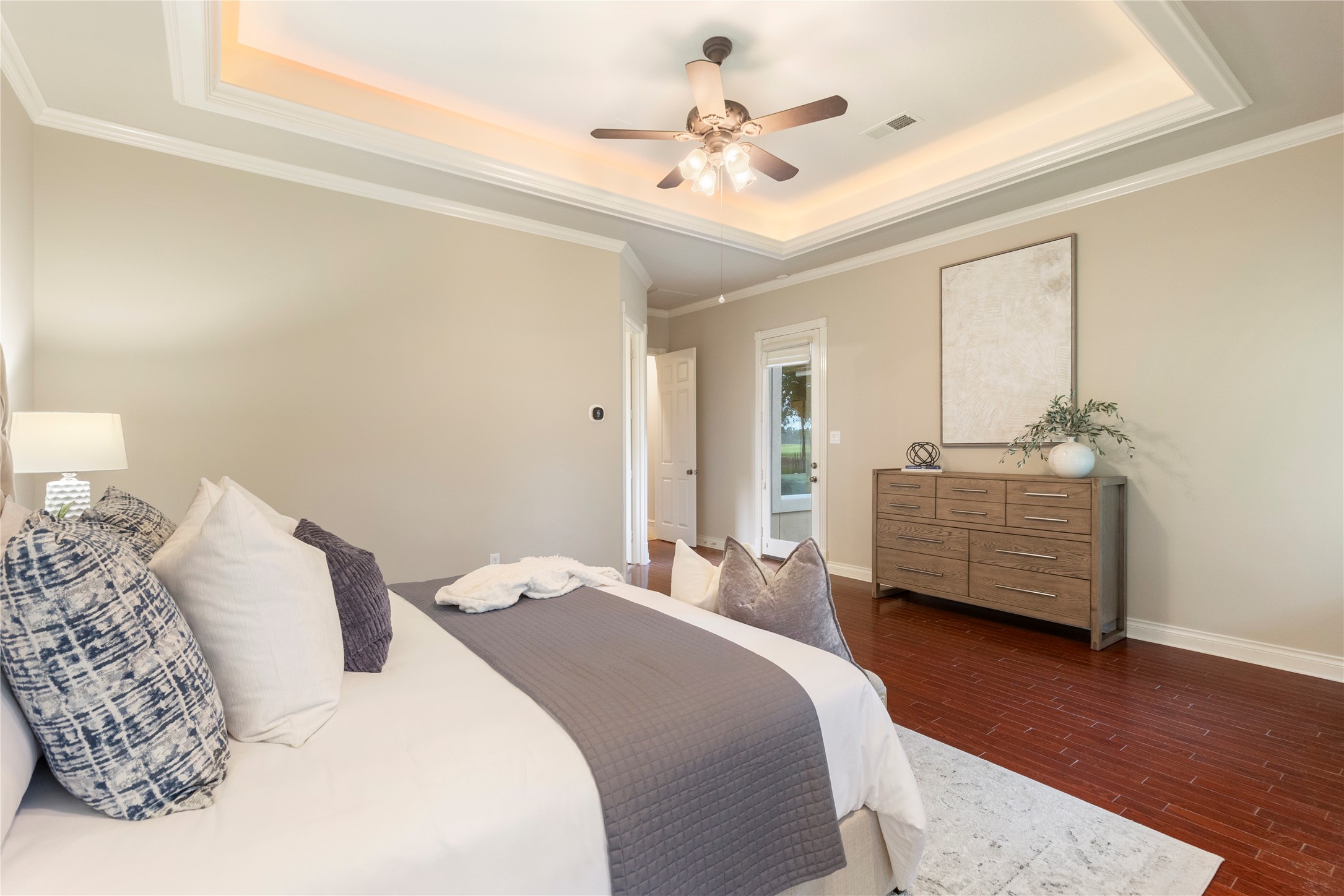 Another angle of the primary suite shows the spacious layout and tray ceiling detail as well as the glass door to your backyard.