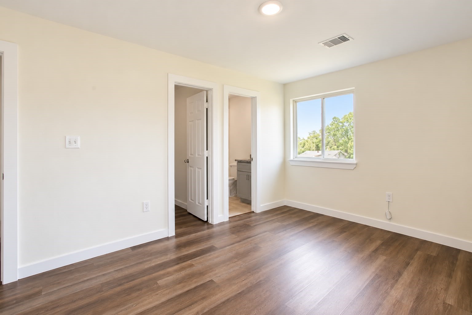 Spacious bedroom with natural light and wood style floors.