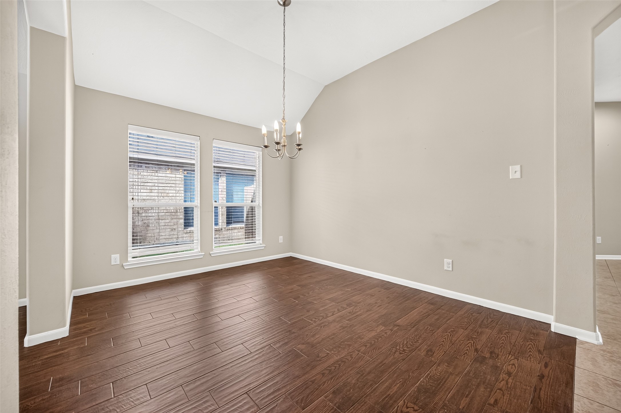 Formal dining room featuring vaulted ceilings, elegant lighting, two large windows, and rich wood-look flooring.