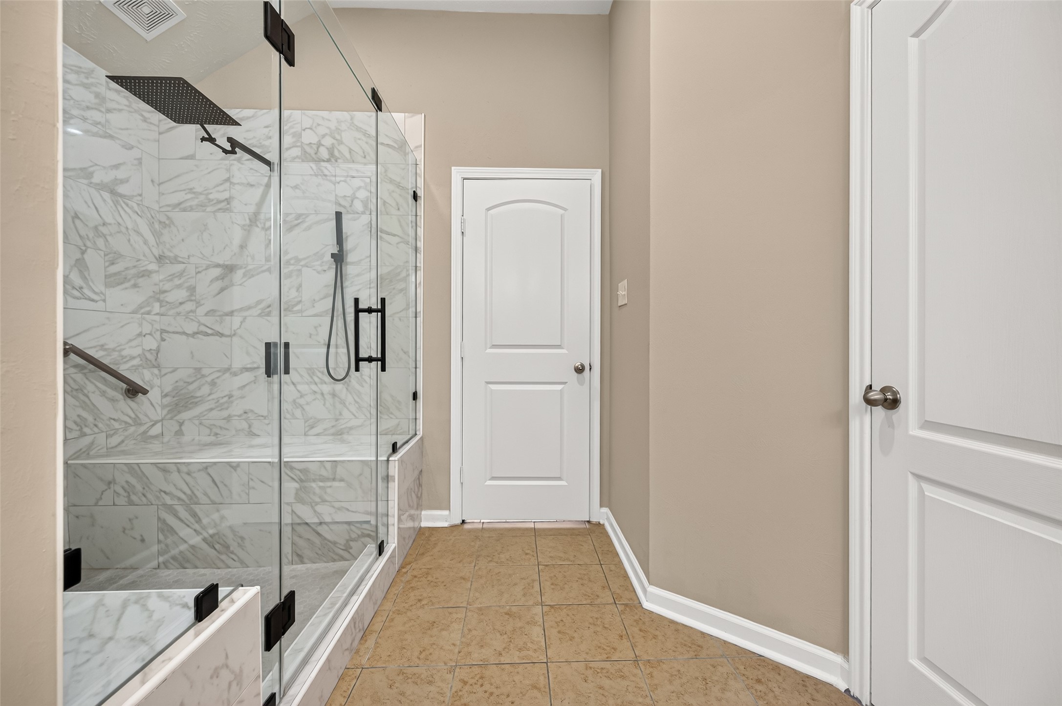 Walk-in shower featuring decorative tilework, a glass enclosure, and built-in shelving.