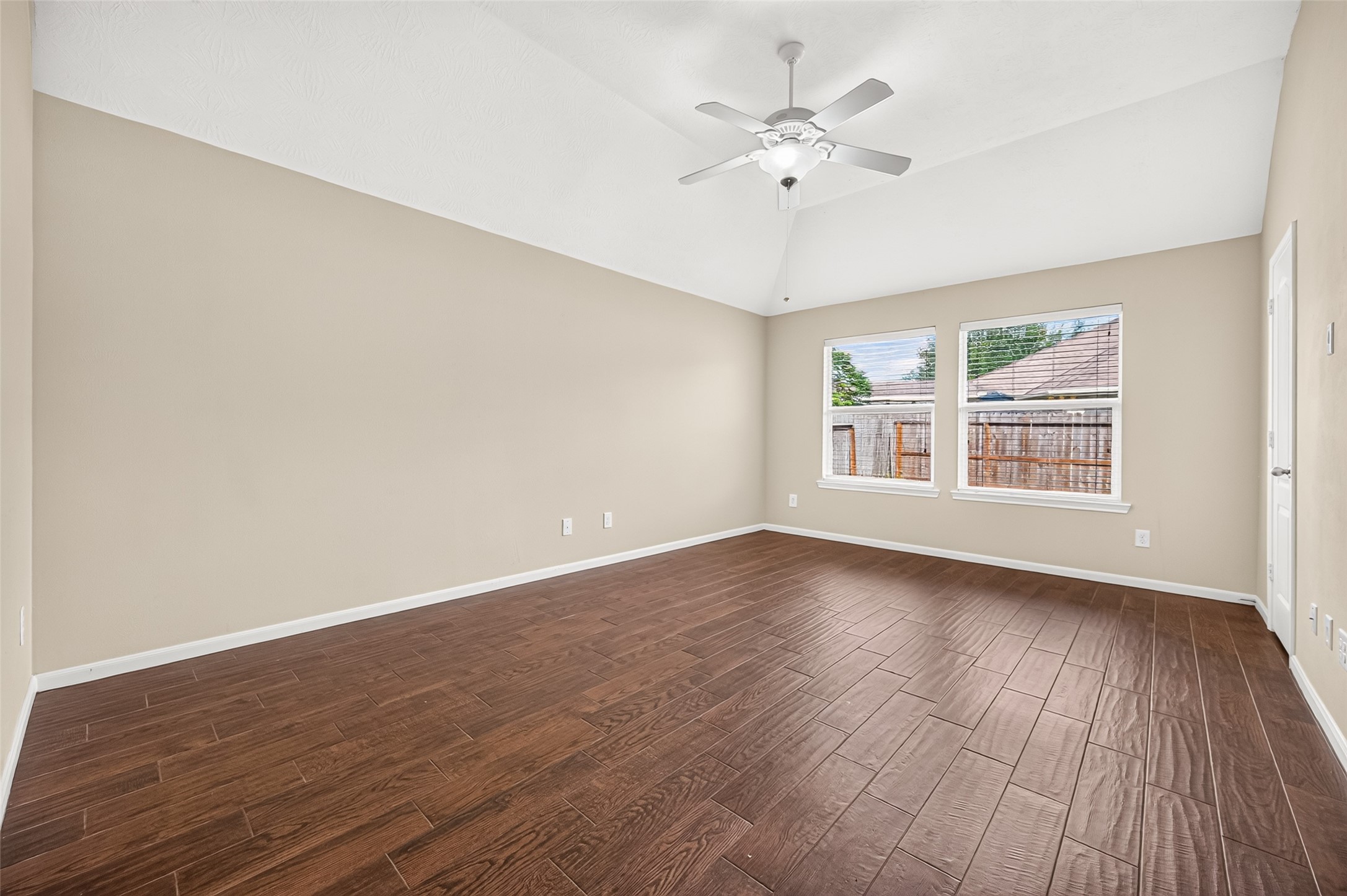 Primary bedroom featuring a vaulted ceiling, ceiling fan, wood-look flooring, and windows overlooking the backyard.