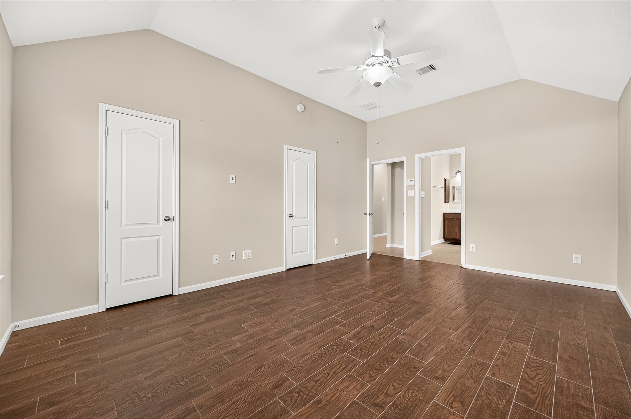 Primary bedroom featuring a vaulted ceiling, ceiling fan, rich wood-look flooring, and access to the adjoining bathroom.