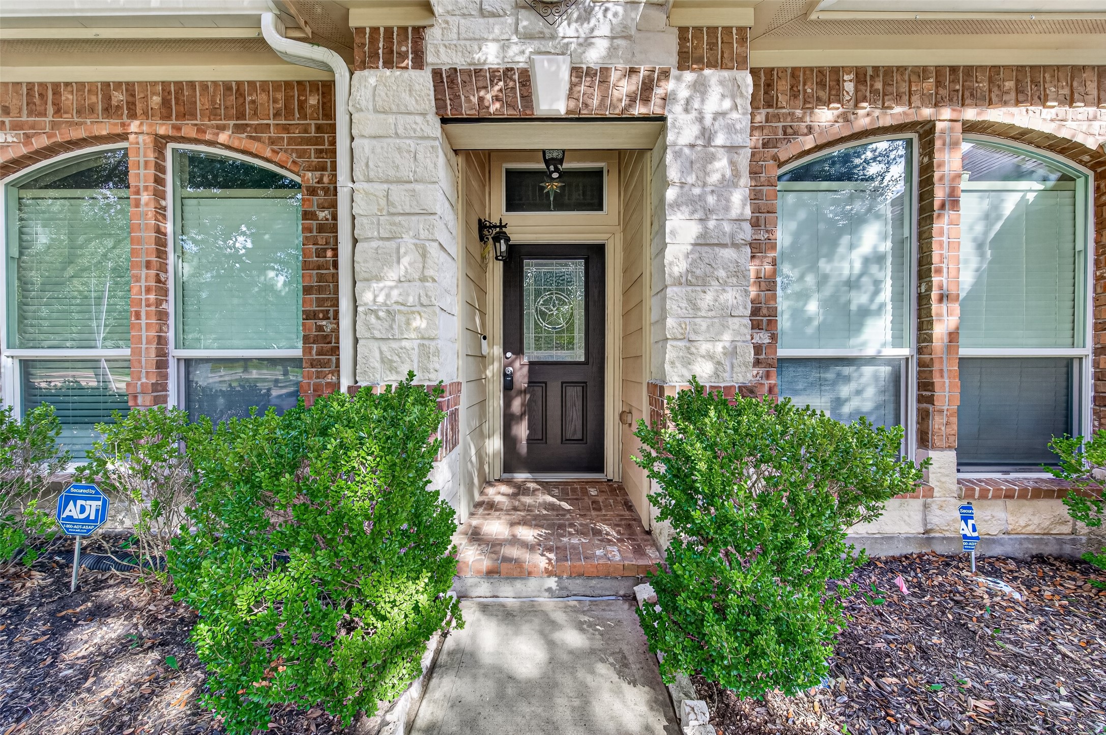 Welcoming front entrance featuring brick detailing, an arched entryway, and landscaped surroundings.