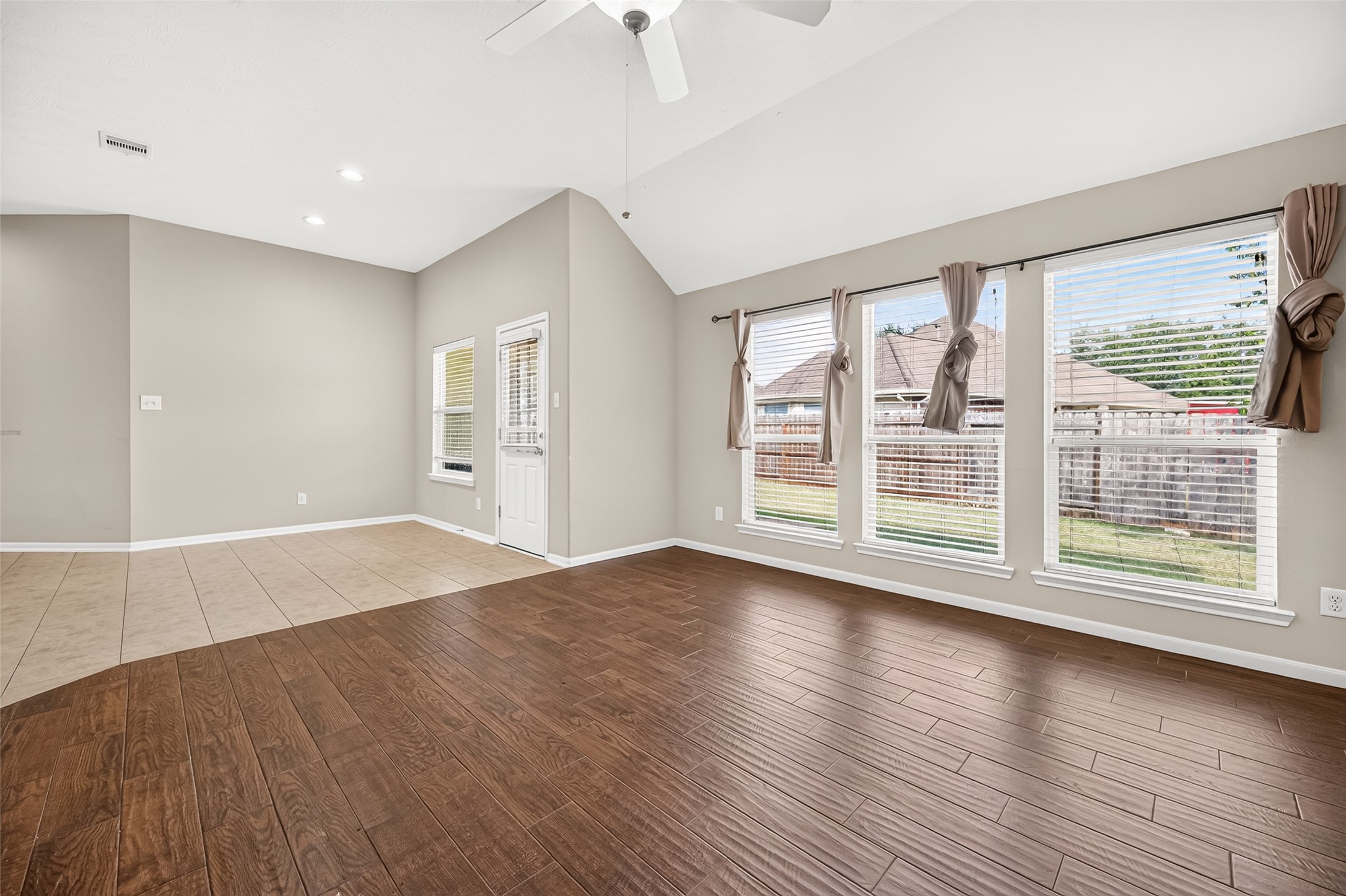 Open living area featuring expansive windows overlooking the backyard and rich wood-look flooring.