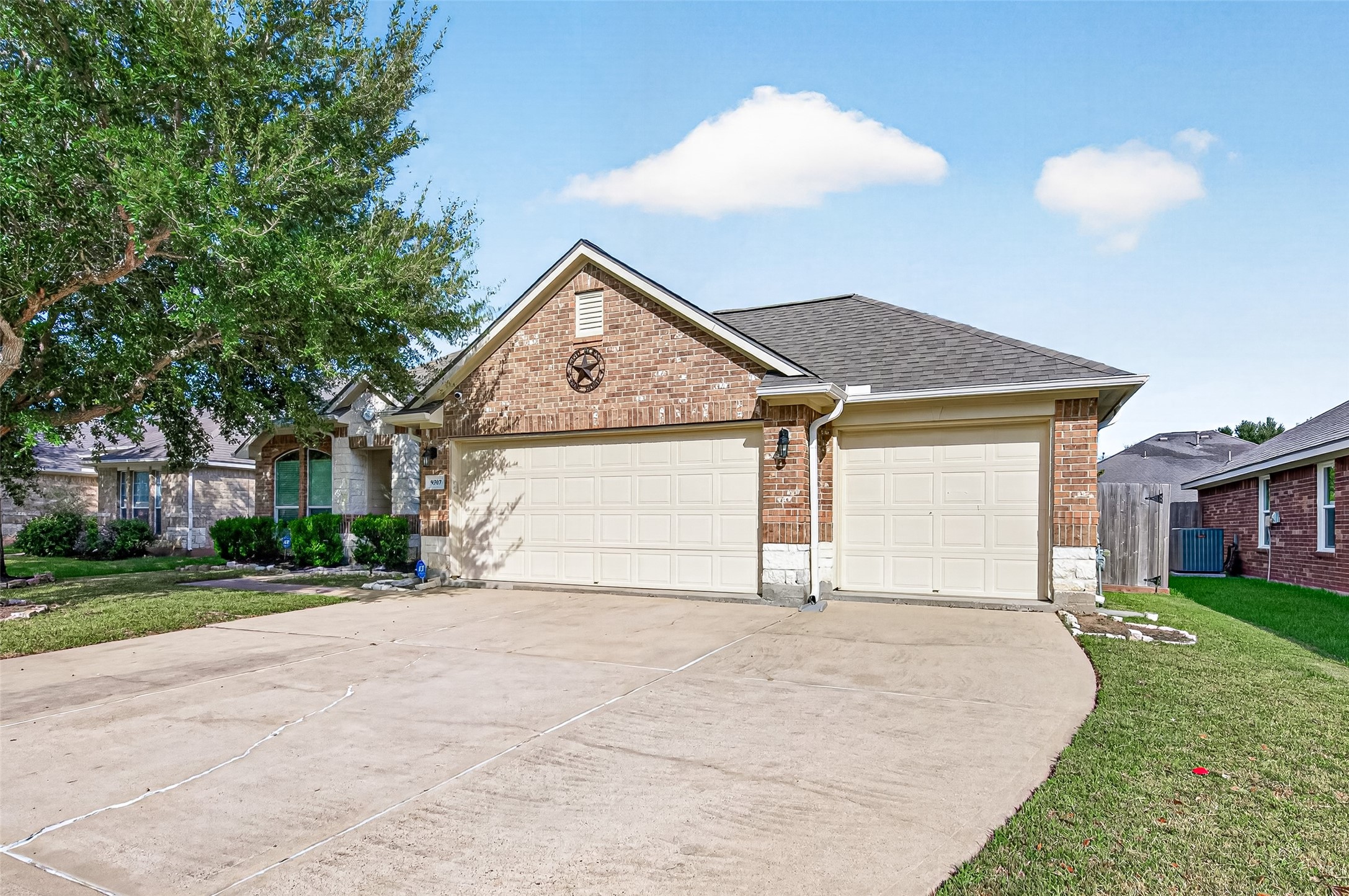 Wide front exterior view showcasing the attached two-car garage, extended driveway, and mature shade trees.