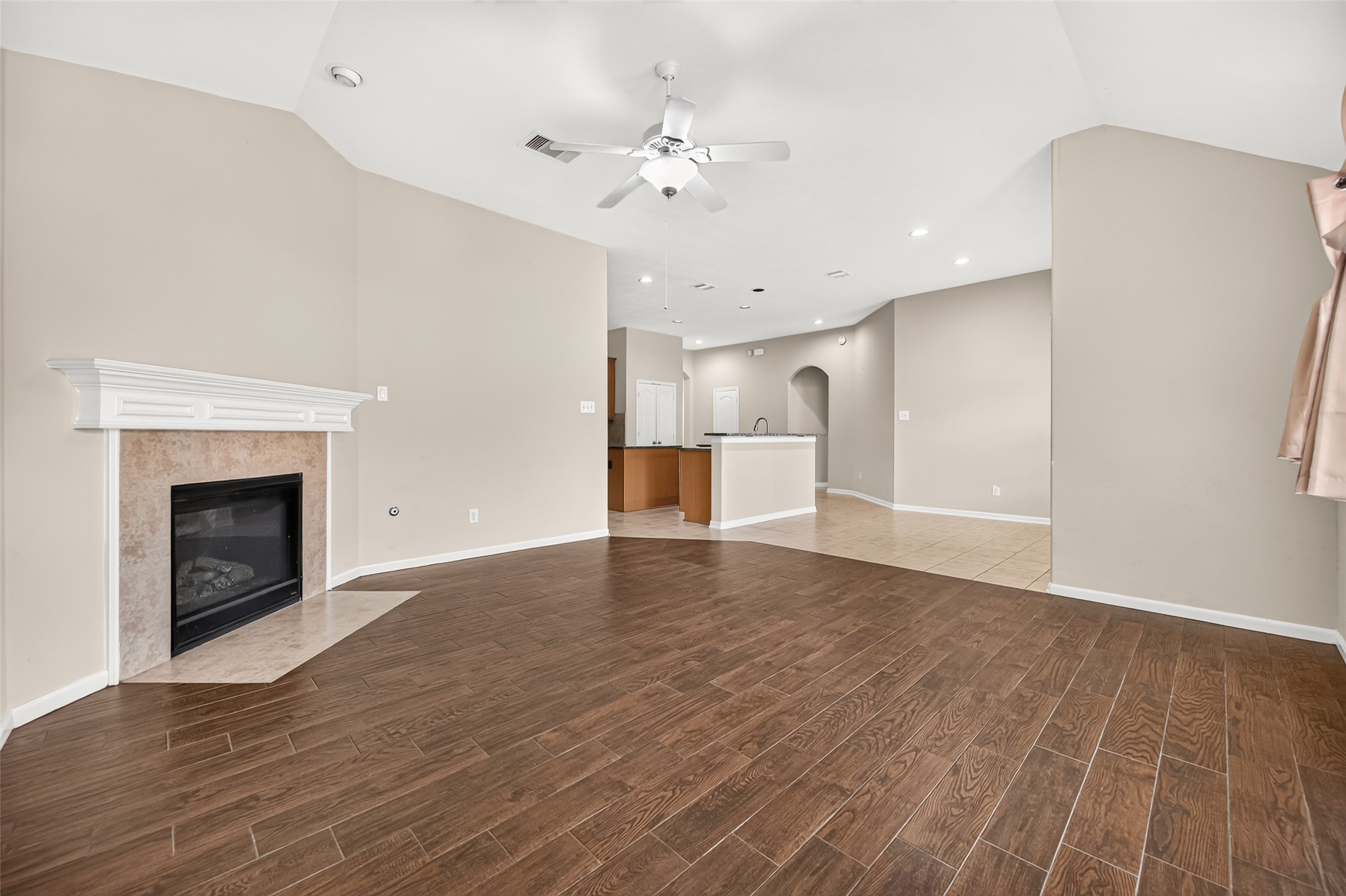 Additional living room view showcasing the fireplace, vaulted ceiling, and seamless connection to the kitchen.