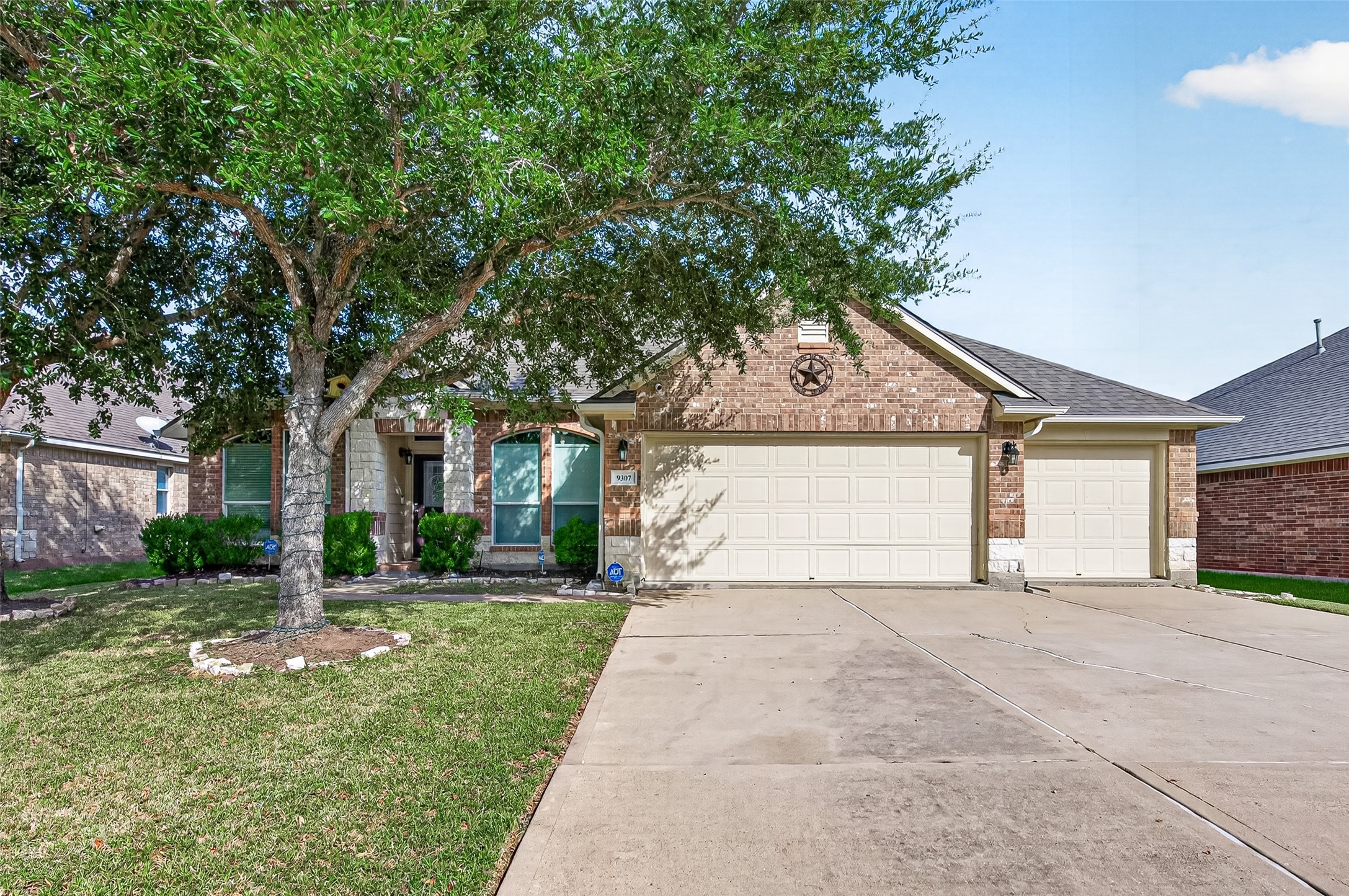 Front exterior showcasing a brick faade, mature trees, a spacious driveway, and an attached two-car garage.