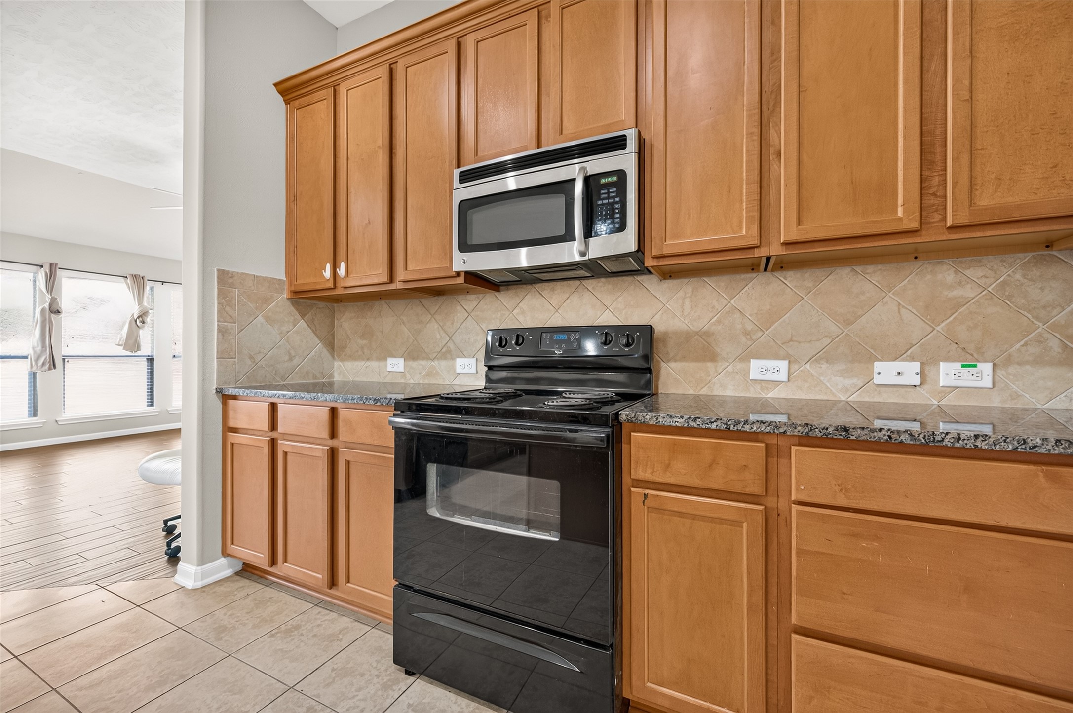 Kitchen featuring wood cabinetry, dark countertops, a tile backsplash, and ample workspace.
