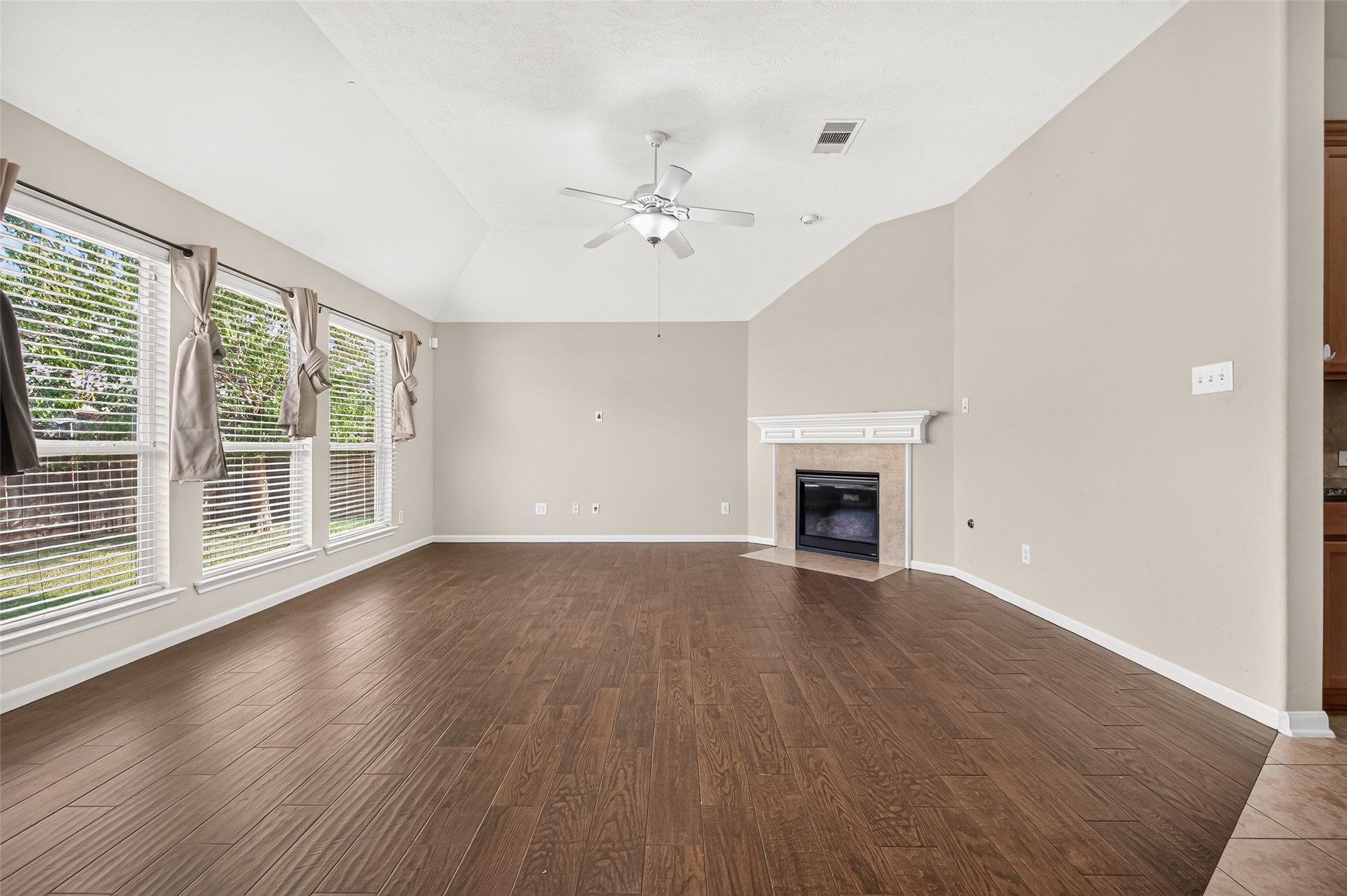 Spacious living room featuring a vaulted ceiling, multiple windows, wood-look flooring, and a fireplace.