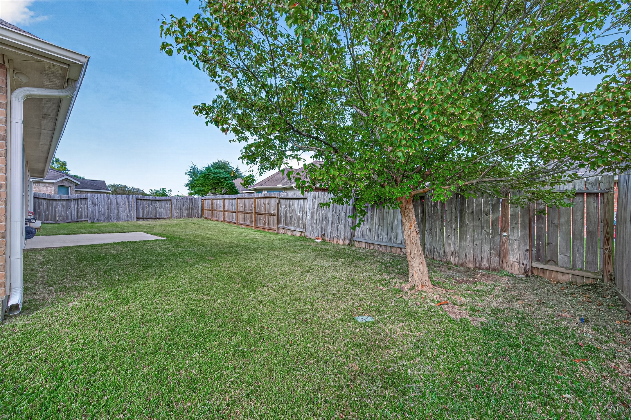 Rear exterior view showcasing the covered patio, brick exterior, and expansive grassy backyard.