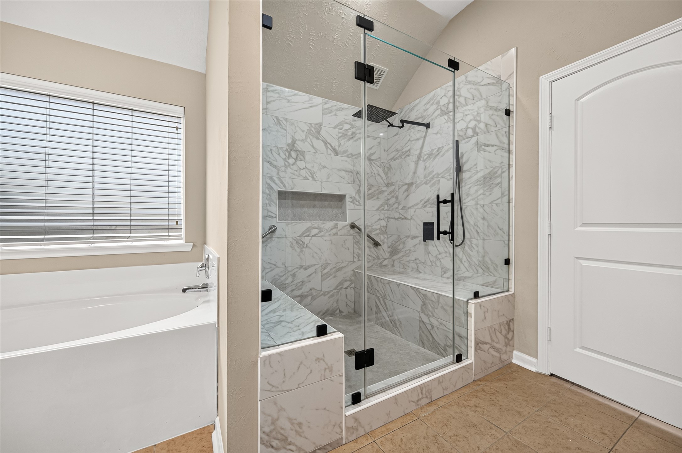 Primary bathroom showcasing the separate soaking tub, glass-enclosed shower, and tiled walls.