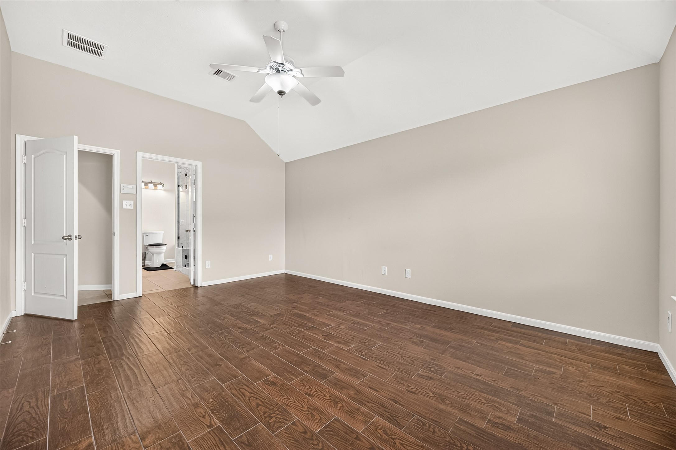Another view of the primary bedroom highlighting its spacious layout, neutral finishes, and vaulted ceiling.