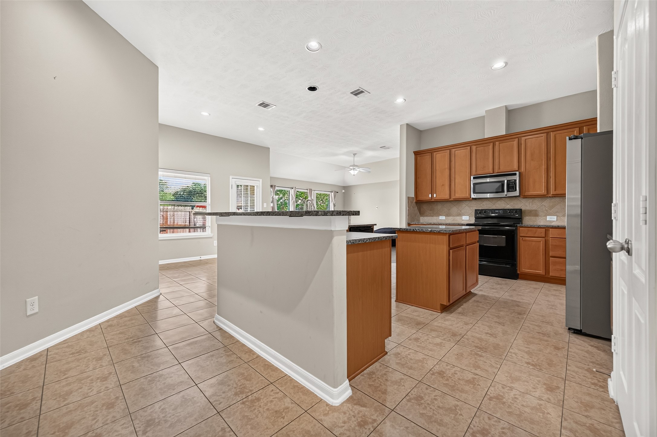 Kitchen featuring a center island, warm wood cabinetry, tile flooring, and an open view into the living area.