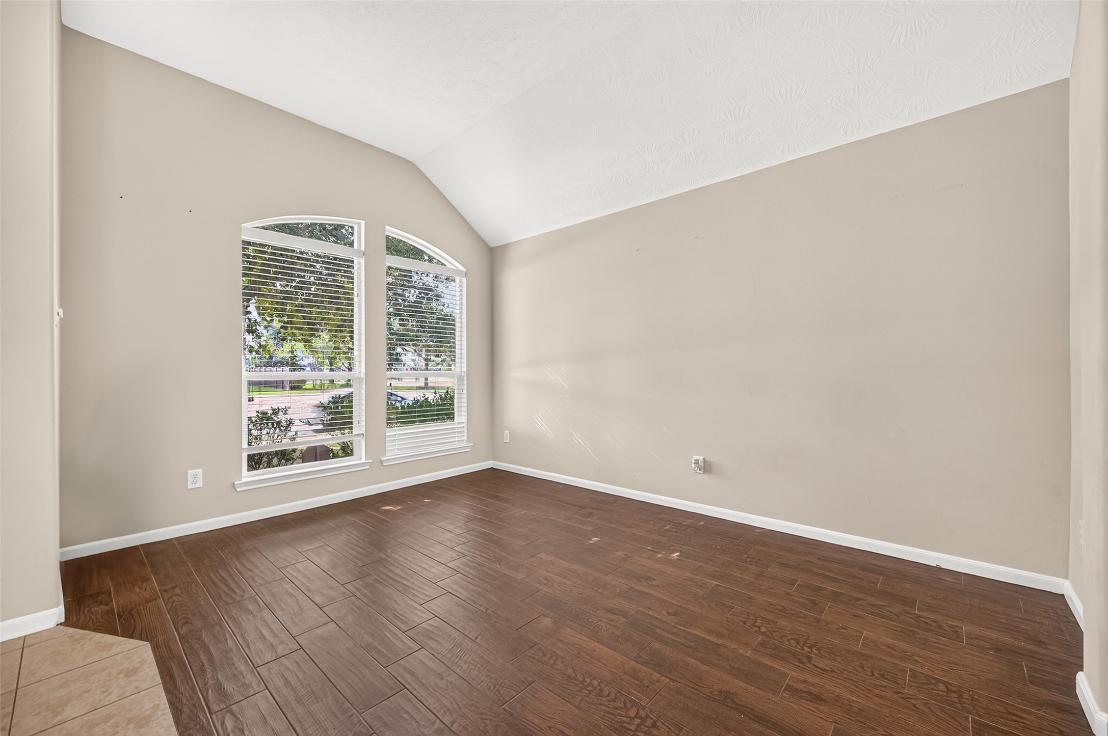 Versatile flex area featuring wood-look flooring, arched windows, and neutral walls, suitable for a variety of uses.