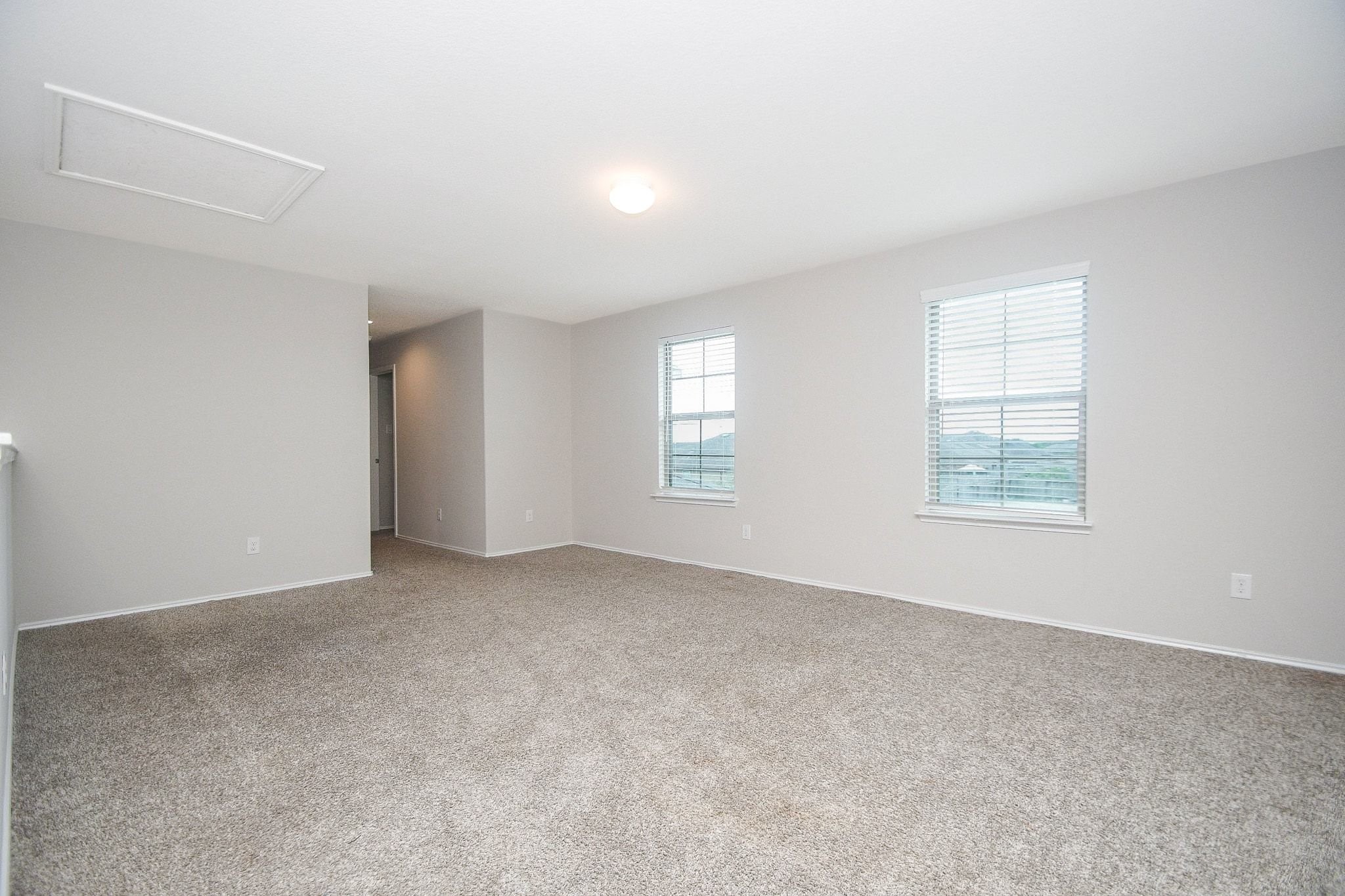 Spacious, carpeted Gameroom upstairs with neutral walls, ample natural light from two windows, and a cozy, inviting atmosphere.