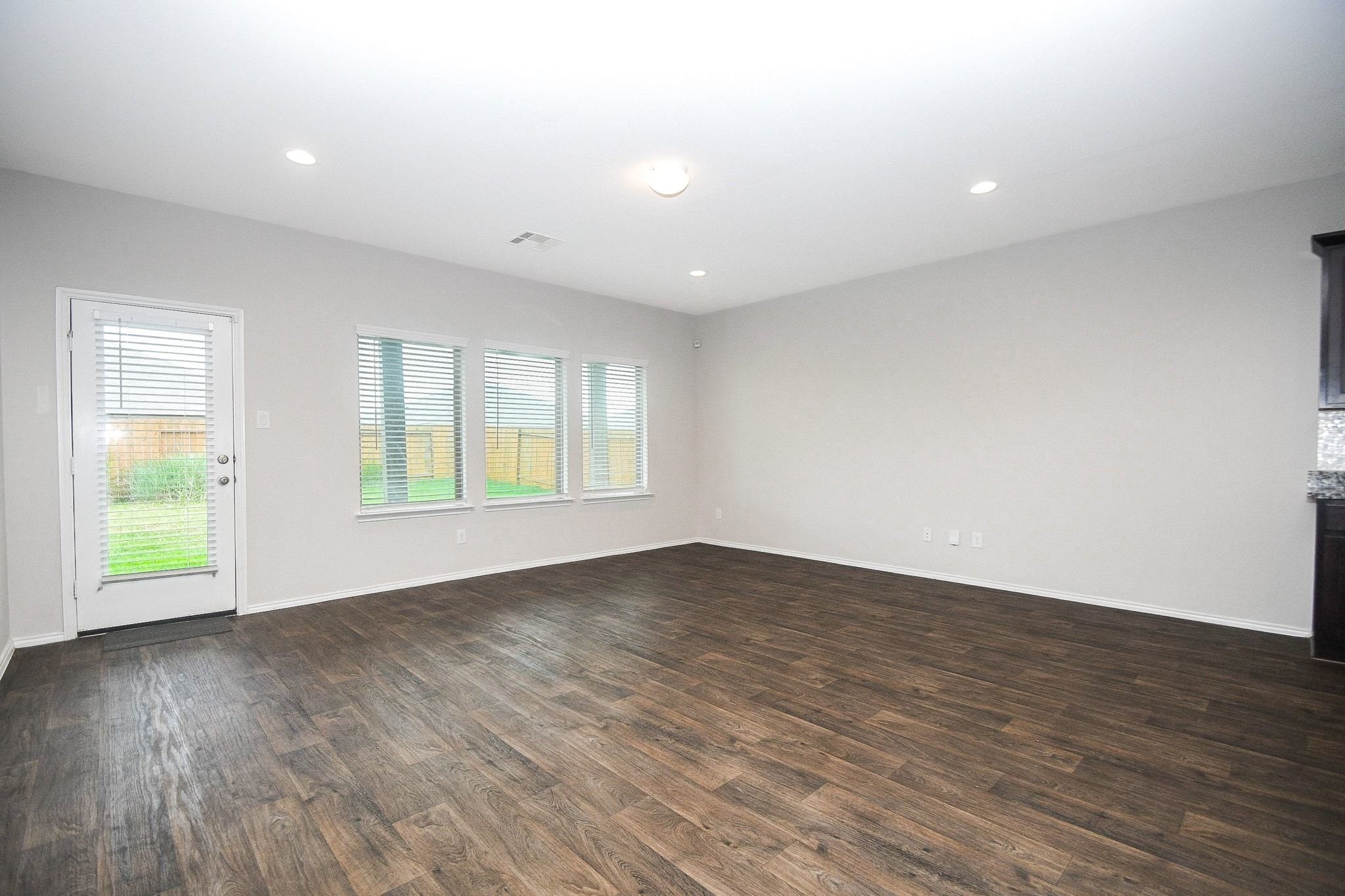 Spacious living area with sleek hardwood floors, abundant natural light from large windows, and a door leading to the backyard.