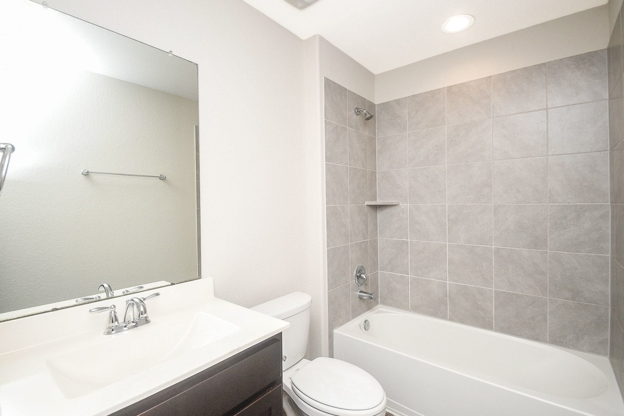 Modern full bathroom upstairs featuring a sleek vanity, large mirror, and a spacious tub with elegant tile surround.