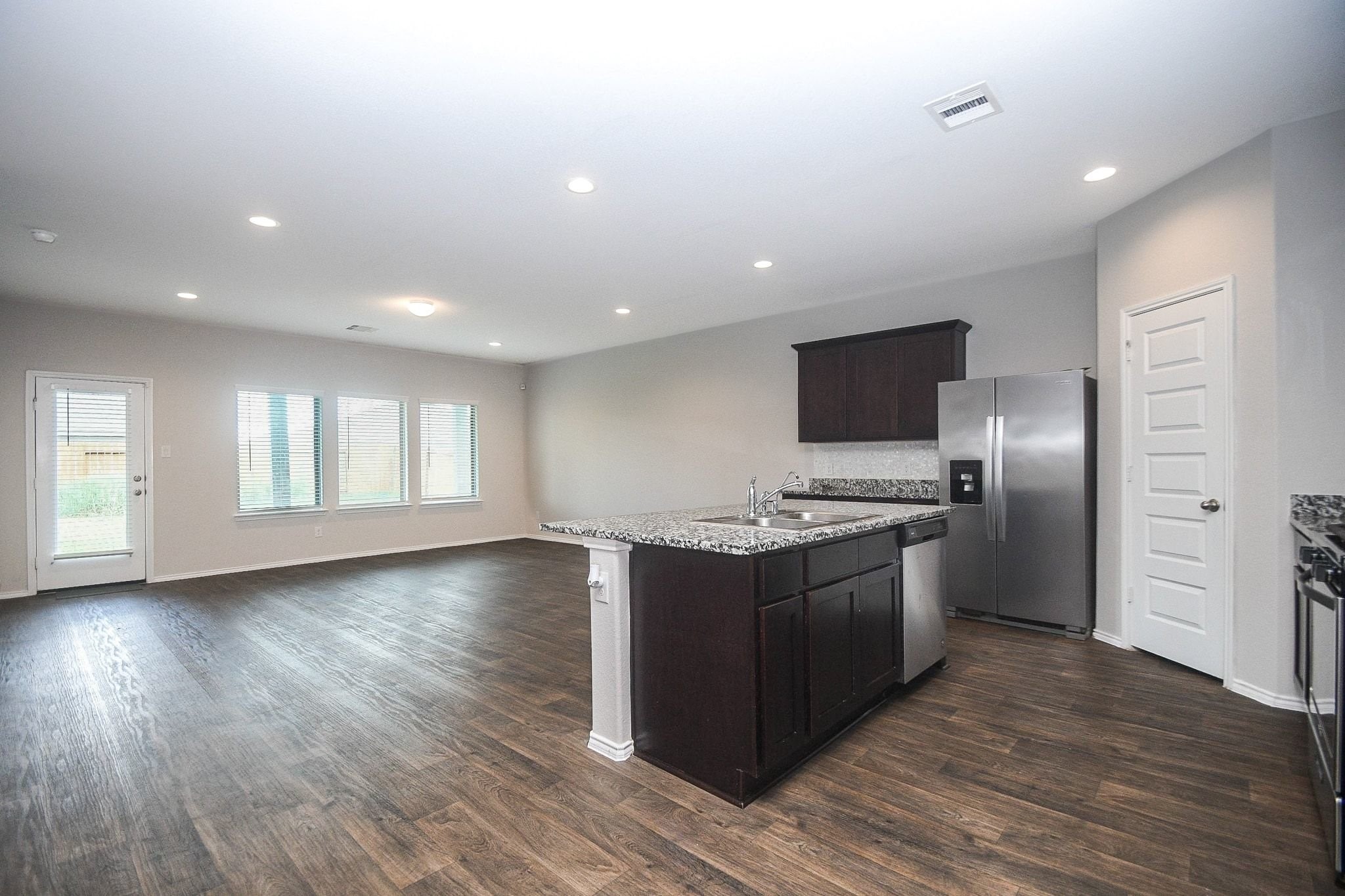 Spacious open-concept living area with sleek hardwood floors, a modern kitchen featuring granite countertops, stainless steel appliances, and abundant natural light from large windows.