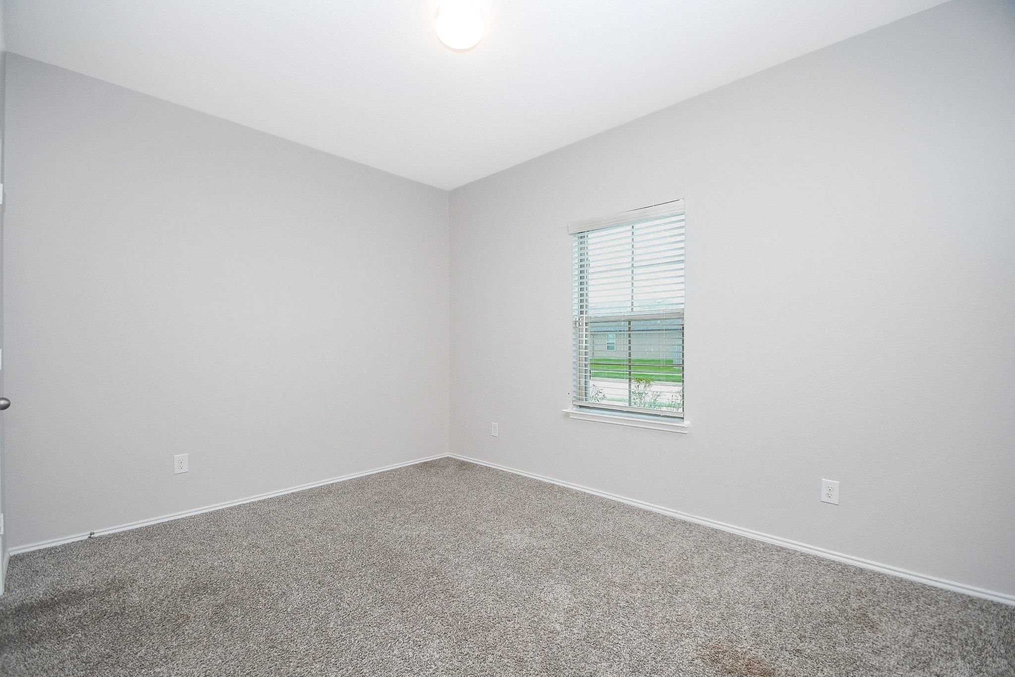 Bright and inviting secondary bedroom downstairs with soft carpeting, neutral walls, and a window providing ample natural light.