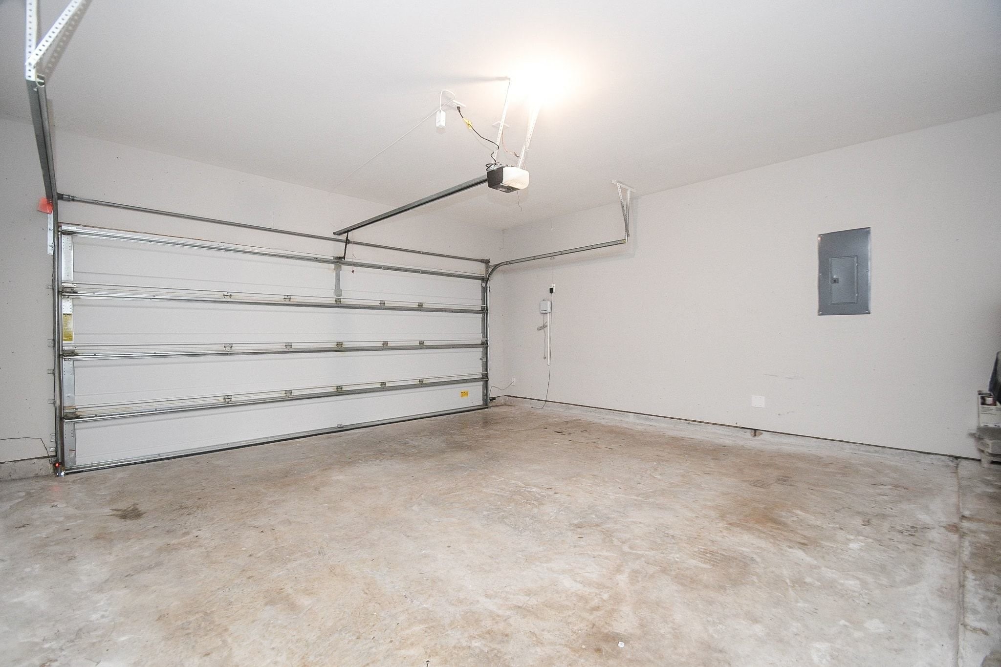 A spacious, well-lit 2 car garage with a clean concrete floor and automatic double-door entry, perfect for parking and storage.