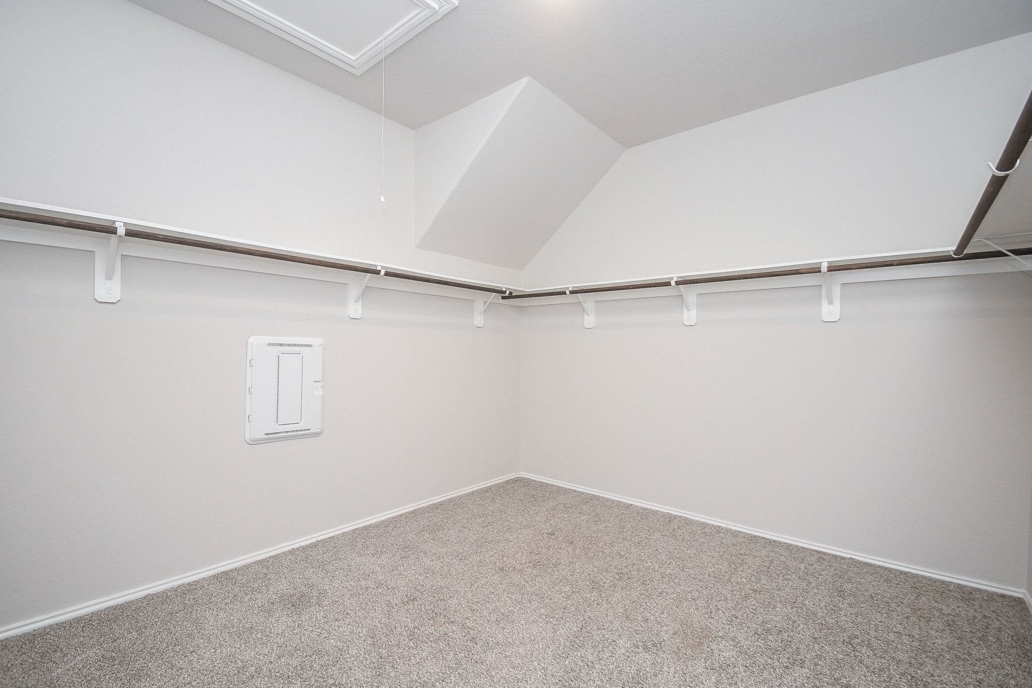 Spacious primary bedroom walk-in closet with ample hanging space and neutral carpeting, perfect for organizing your wardrobe.