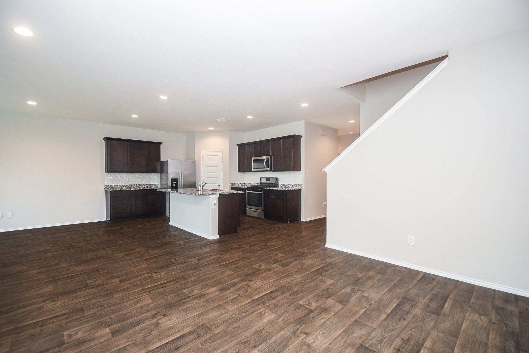 Spacious open-concept living area with modern kitchen, featuring dark wood cabinets, stainless steel appliances, and elegant granite countertops, complemented by rich wood flooring.