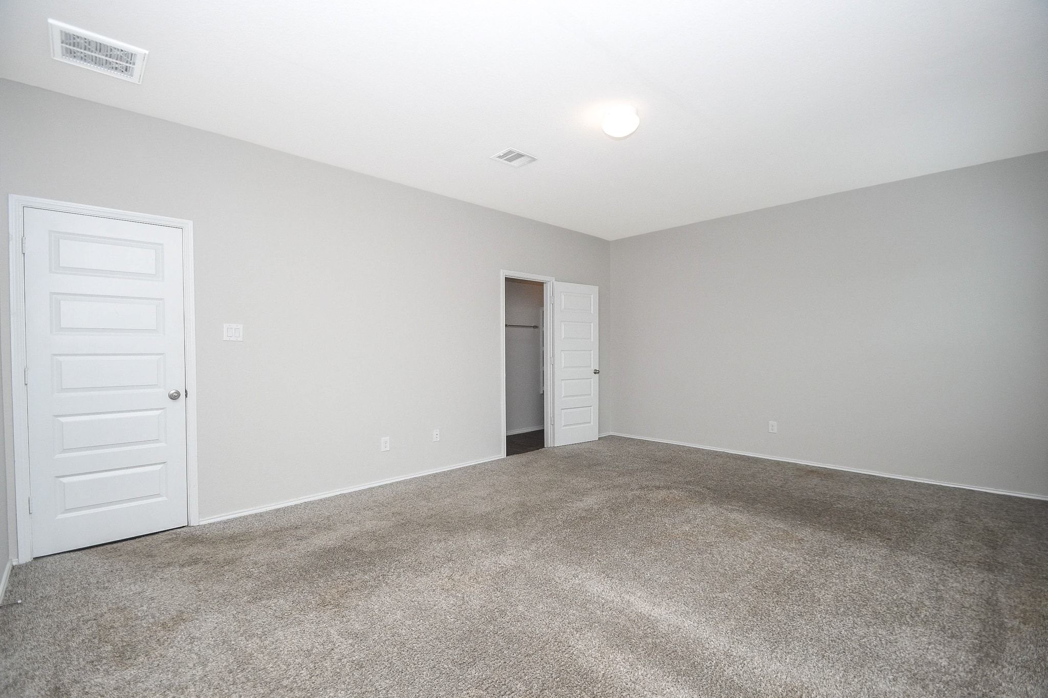 Another view of the spacious primary bedroom with neutral walls, plush carpeting, and ample natural light, featuring closet for convenient storage.