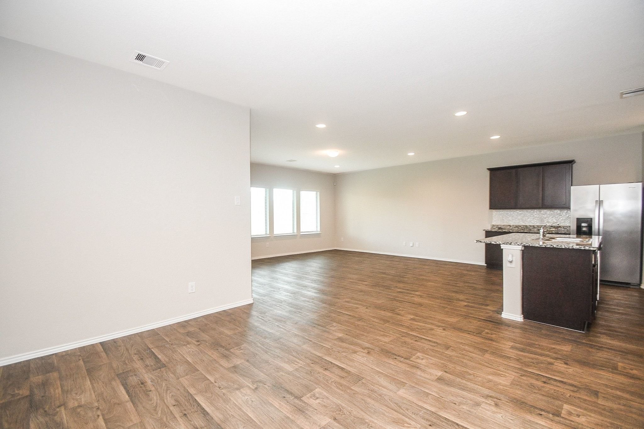 Spacious open-concept living area with rich hardwood flooring, recessed lighting, and a modern kitchen featuring granite countertops and stainless steel appliances.