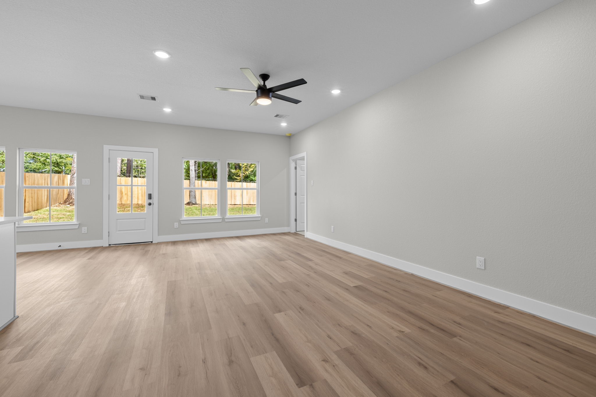 Large family room with LVP floors, ceiling fan and wall of windows