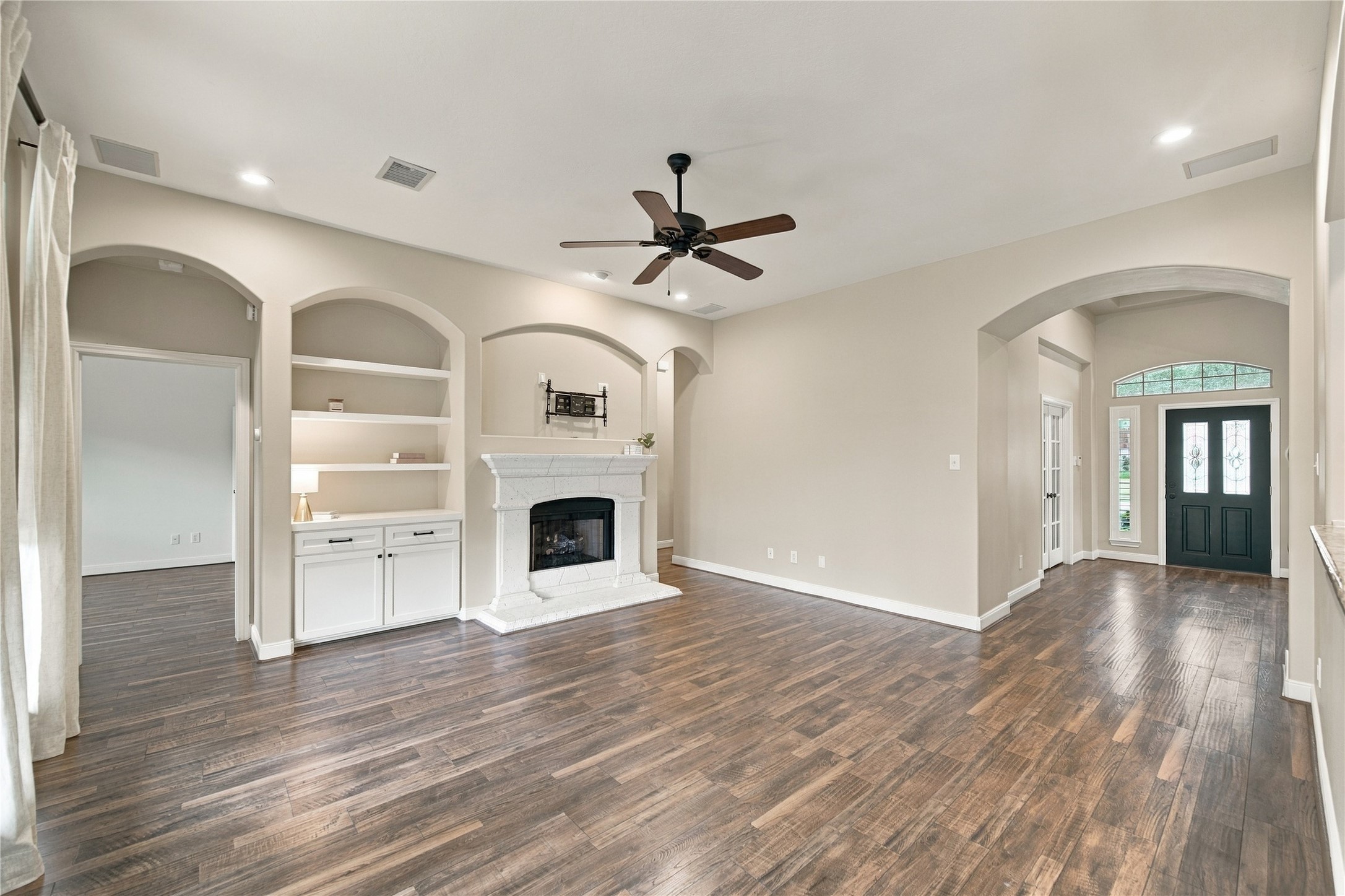 From this view of the family room, you'll see the doorway to the primary bedroom suite on the left, offering convenient access and separation from the secondary bedrooms. Notice the beautiful arched openings, built-in shelving, and cozy gas fireplace!