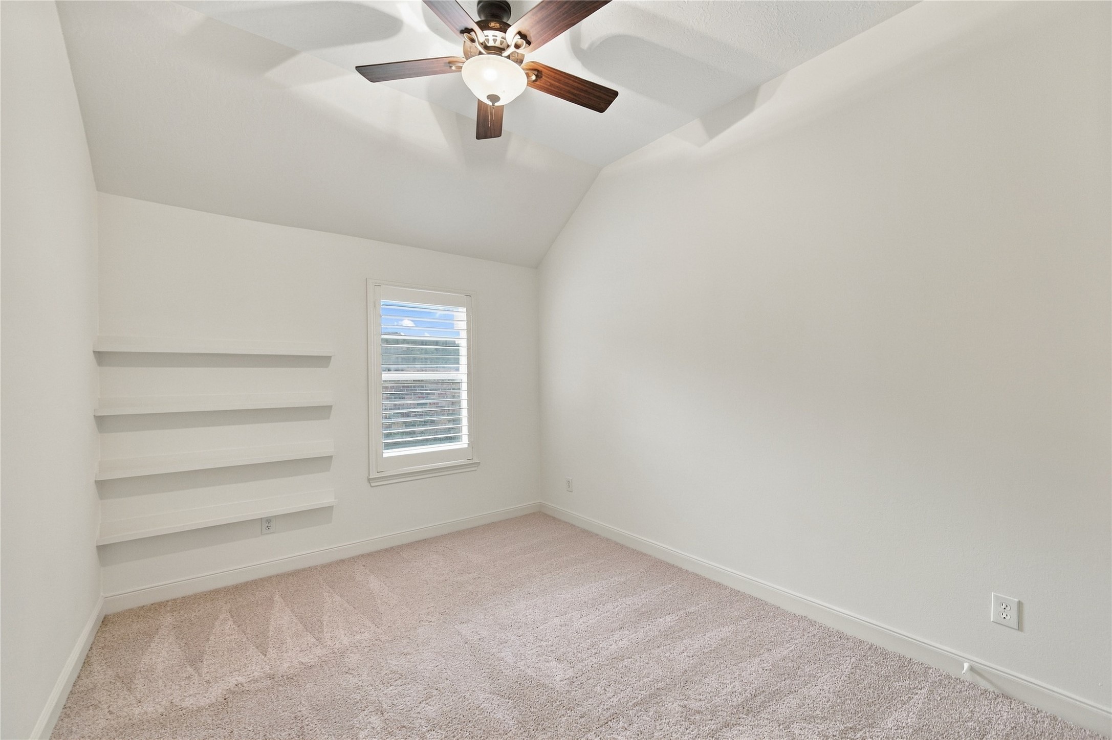 This charming secondary bedroom features a vaulted ceiling, plantation shutters, new carpet, and built-in book rails, perfect for displaying favorite books and keeping them within easy reach.