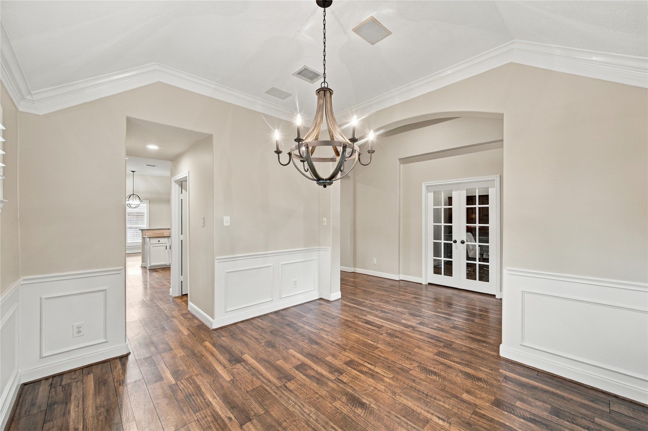 From this angle of the dining room, you can appreciate the home's thoughtfully planned architectural details, including elegant arched openings, beautiful crown molding, and decorative wall paneling. The rich wood-look flooring adds warmth and character. From this angle of the dining room, you can appreciate the home's thoughtfully planned architectural details, including elegant arched openings, beautiful crown molding, and decorative wall paneling. The rich wood-look flooring adds warmth and character.