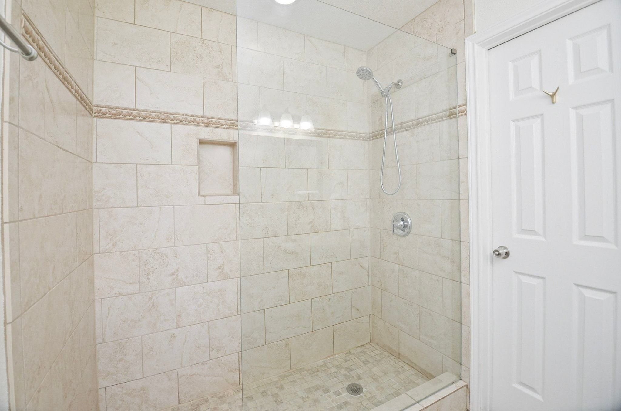 Walk-in shower that boasts neutral earth tones, with half glass door and built-in niche for bath essentials!