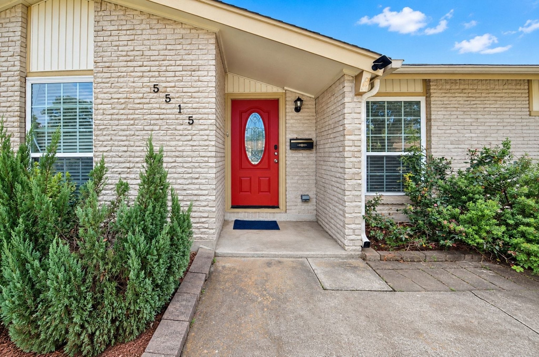 Welcoming mid-century entryway with a bold red front door & light brick exterior.