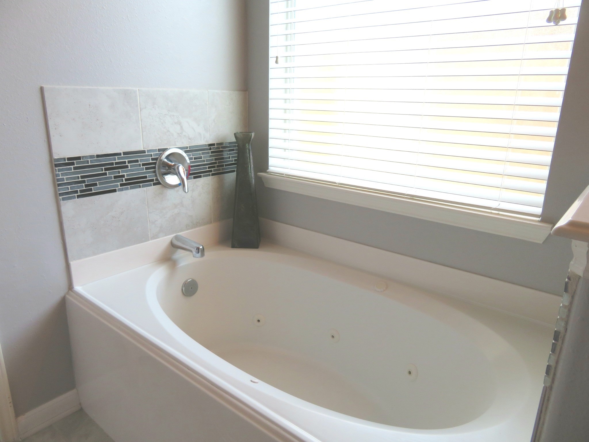 Relax in the elegant bathroom featuring a luxurious jetted tub, complemented by modern tile accents and abundant natural light.