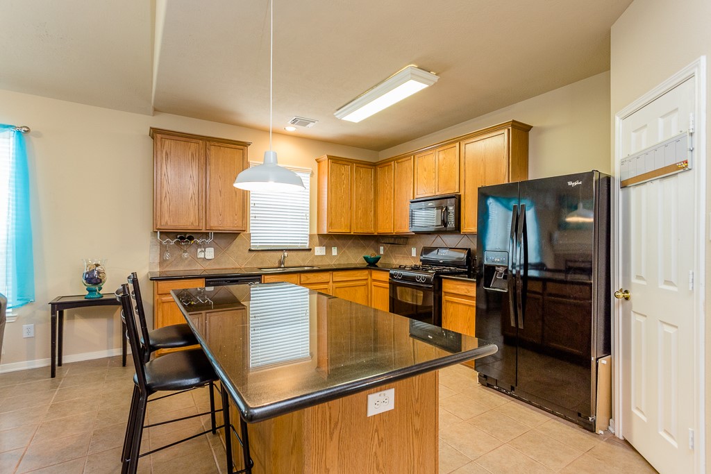 Spacious kitchen featuring sleek black appliances, a large island with seating, and ample wood cabinetry for storage.
