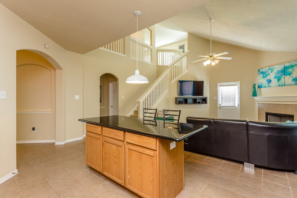 Spacious living area with high ceilings, featuring a modern kitchen island, cozy fireplace, and a  staircase leading to the upper level.