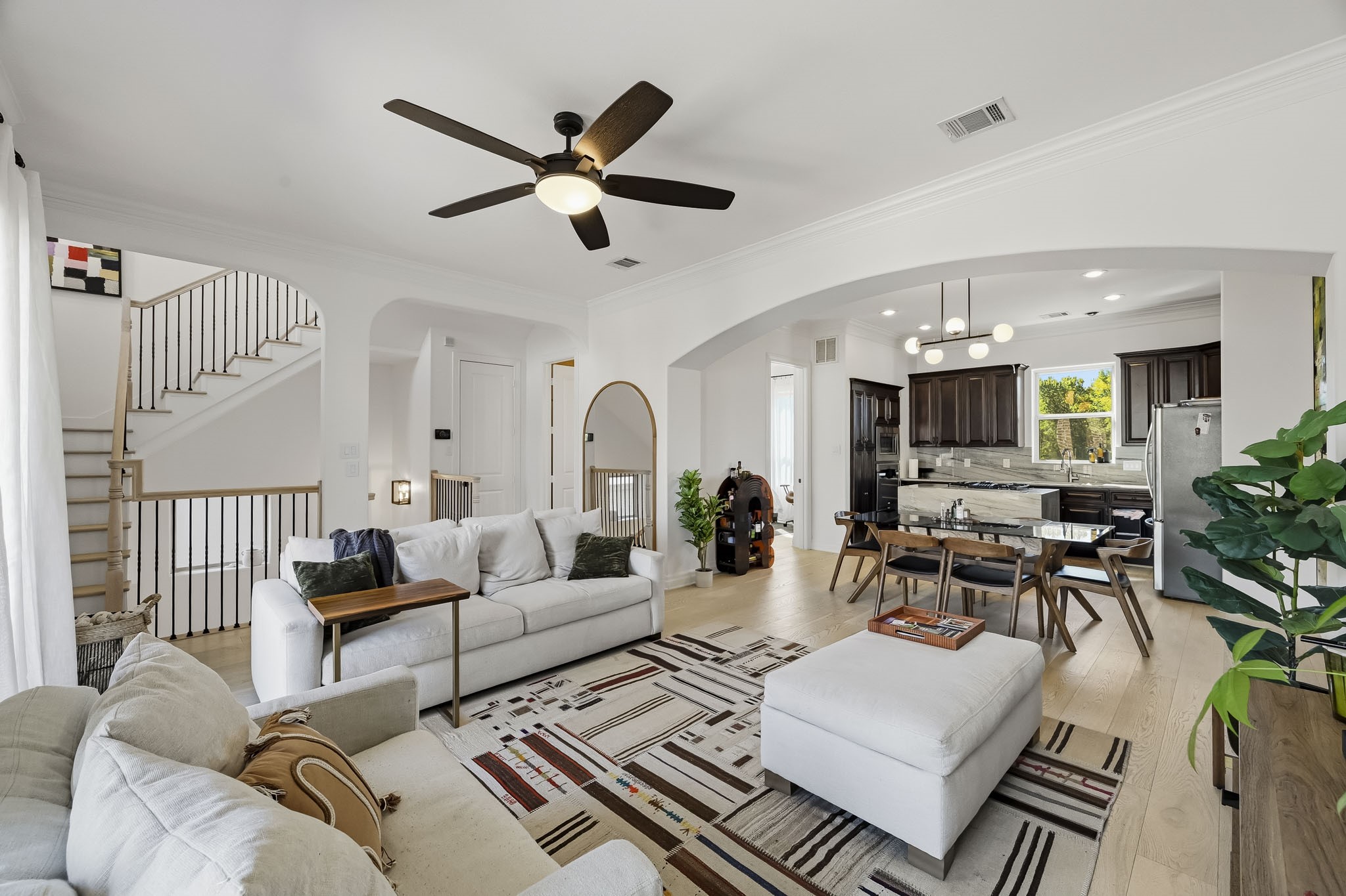 Spacious open-concept living area with modern kitchen, cozy seating, light wood floors, and elegant staircase, perfect for entertaining and relaxation.