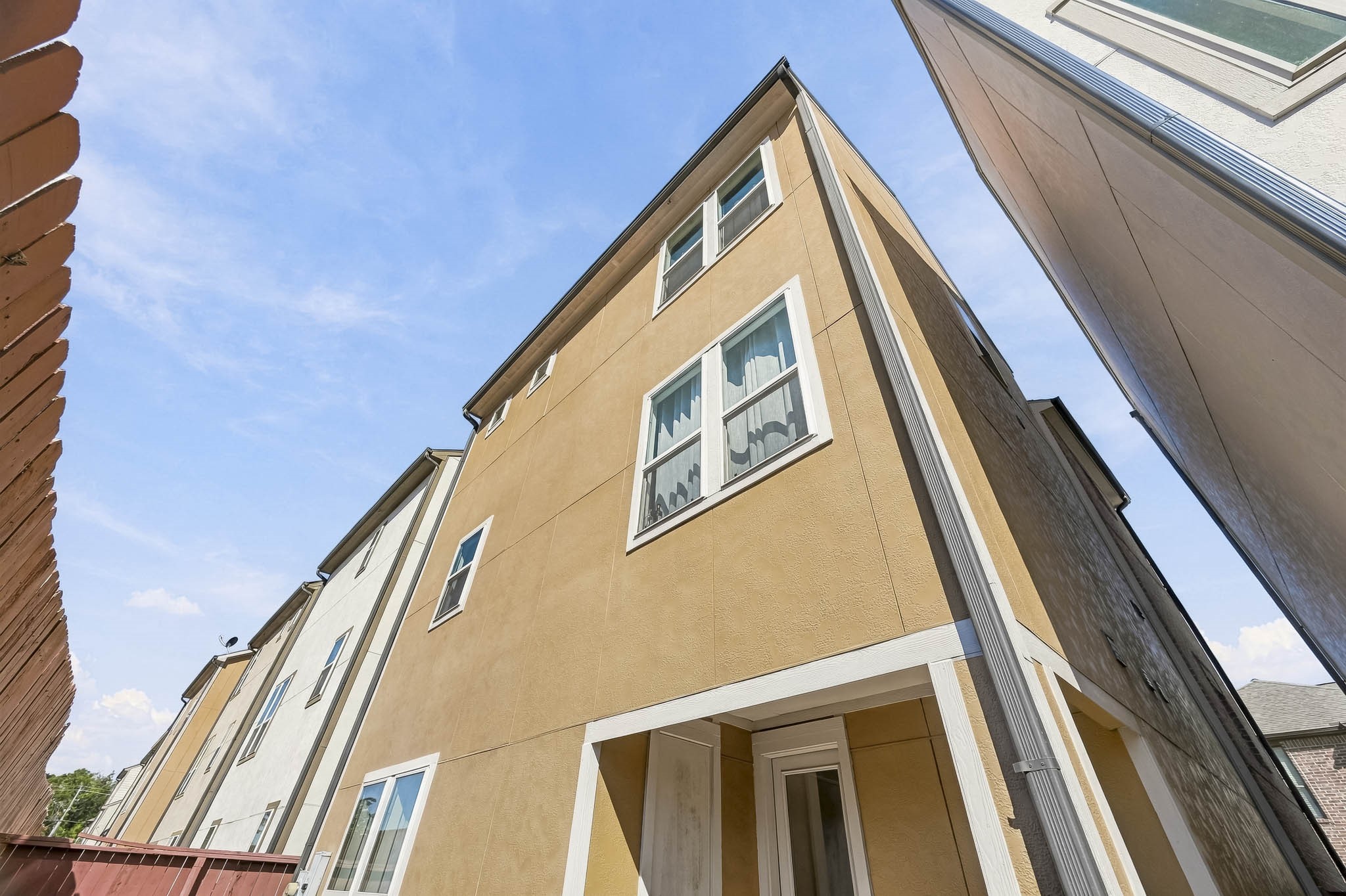 Modern three-story townhouse with a sleek exterior, featuring large windows and a private entrance, nestled in a cozy urban setting.