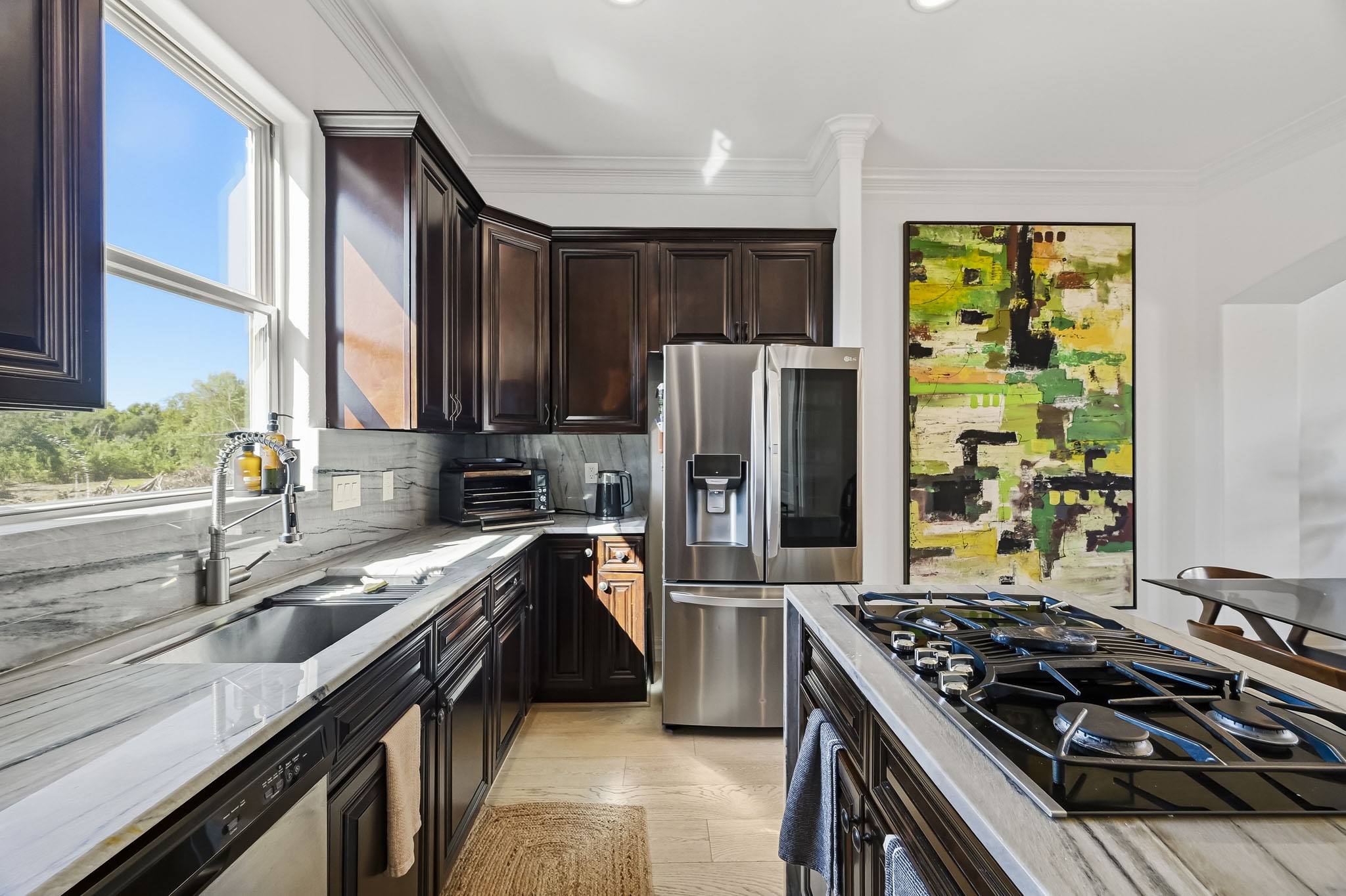 Elegant kitchen featuring rich dark wood cabinetry, modern stainless steel appliances, and a stylish gas cooktop, complemented by a large window that brings in abundant natural light.