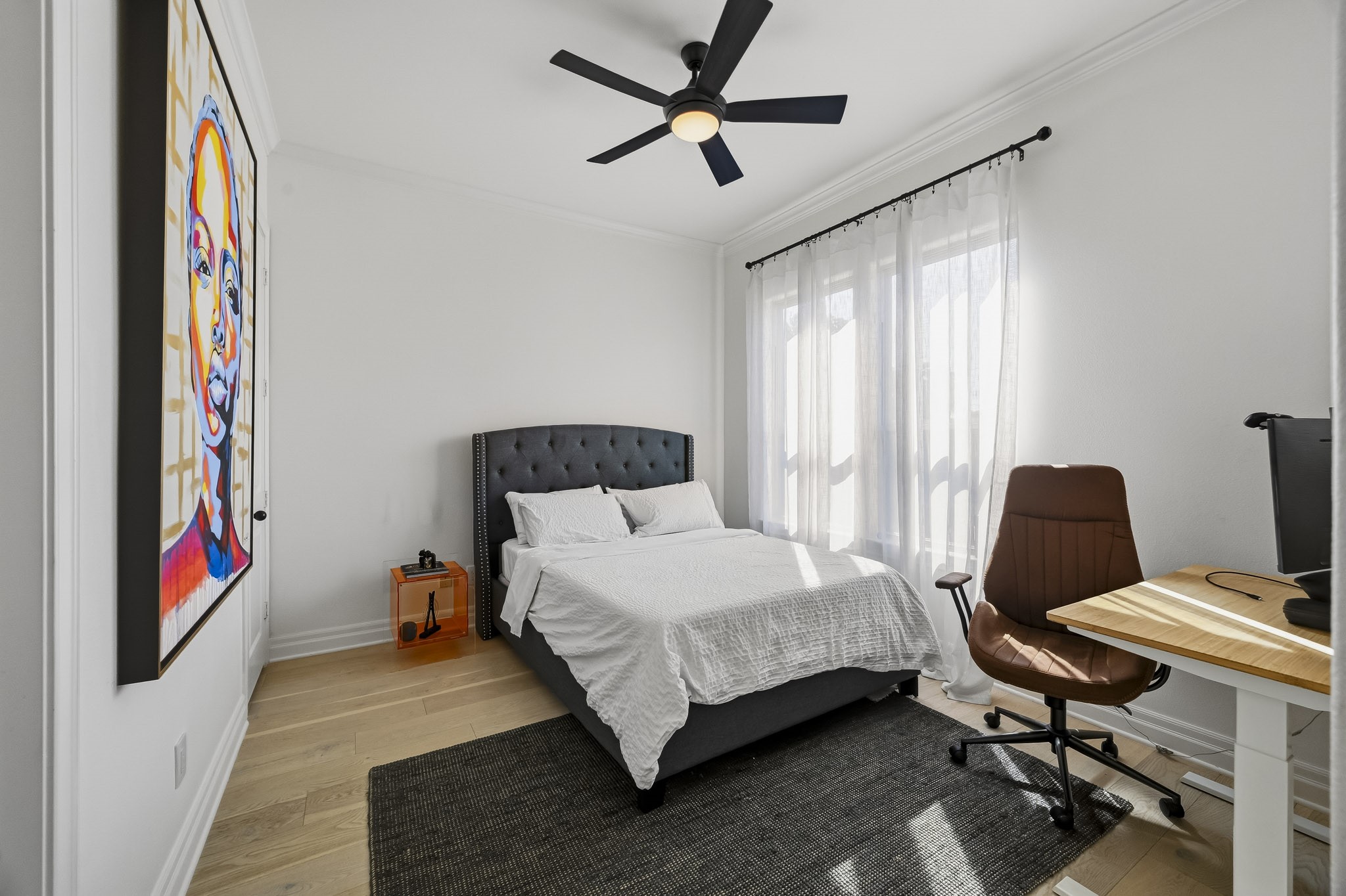 Bright and modern bedroom featuring a large window and a functional workspace with a sleek desk and chair.