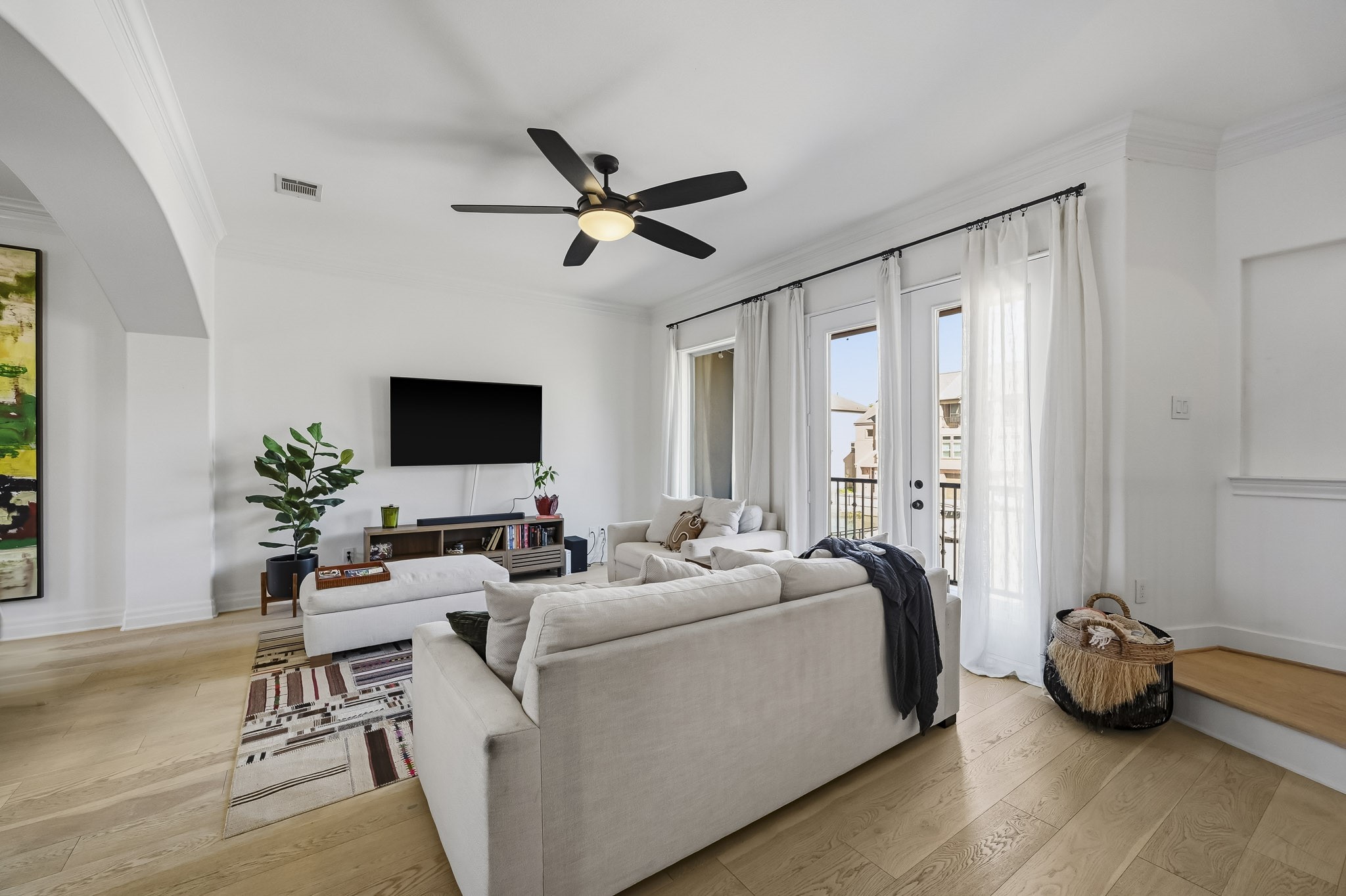 Bright and airy living room featuring a cozy sectional sofa, and floor-to-ceiling windows with sheer curtains, leading to a charming balcony.