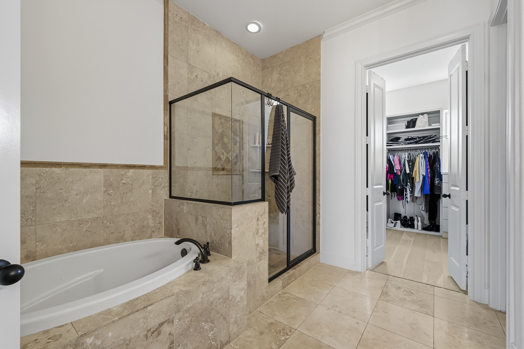 Luxurious bathroom featuring a spacious soaking tub and a sleek glass-enclosed shower, seamlessly connected to a generous walk-in closet with ample storage space.