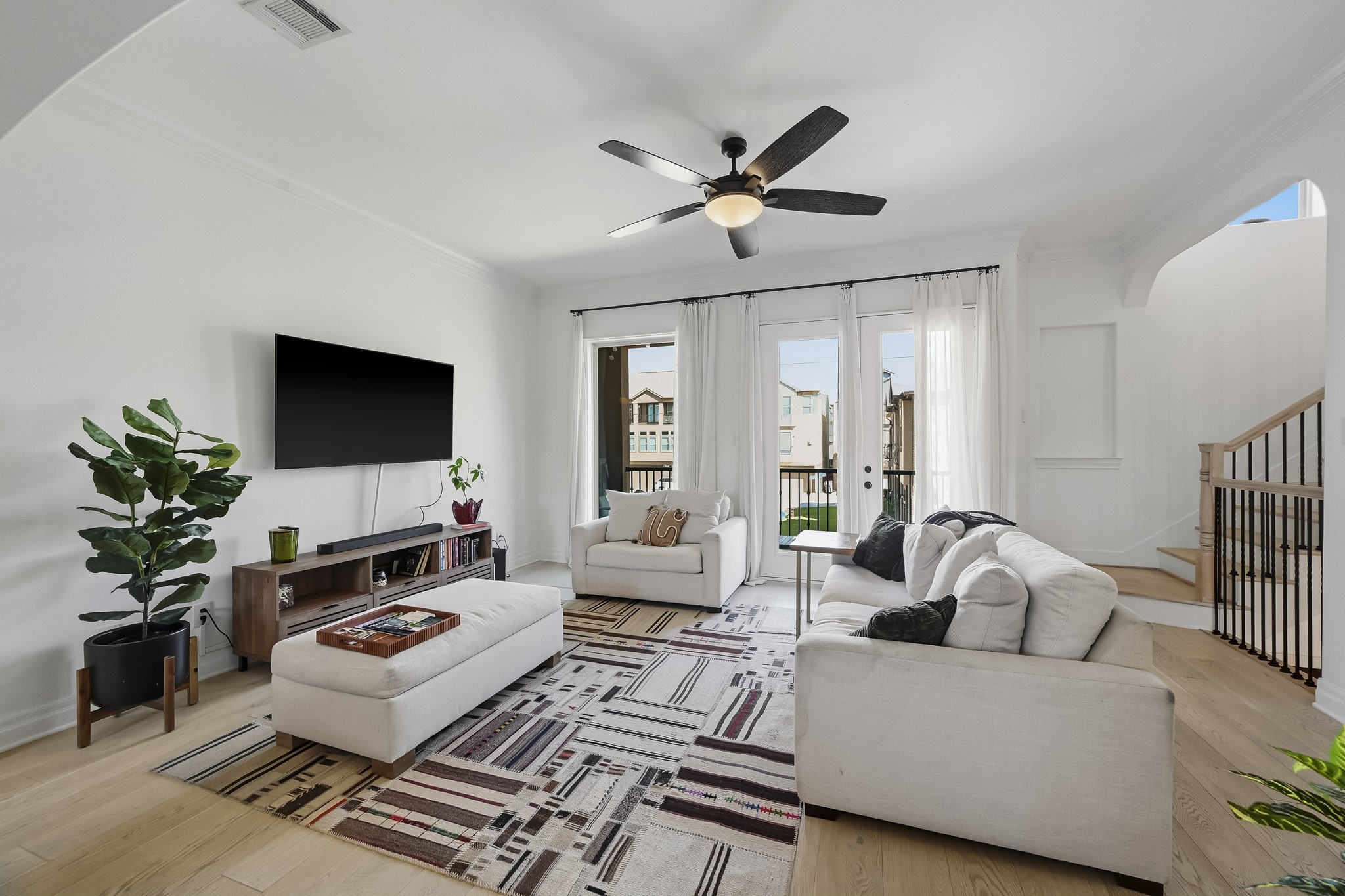 Bright and inviting living room with elegant hardwood floors and abundant natural light streaming through glass doors, leading to a charming outdoor view.