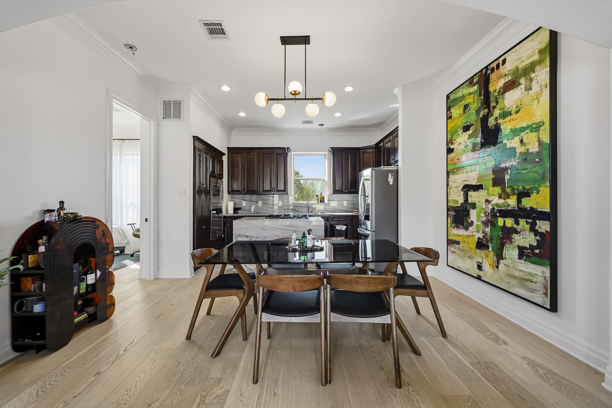 Stylish dining area with contemporary lighting, adjacent to a modern kitchen featuring dark wood cabinetry and stainless steel appliances.