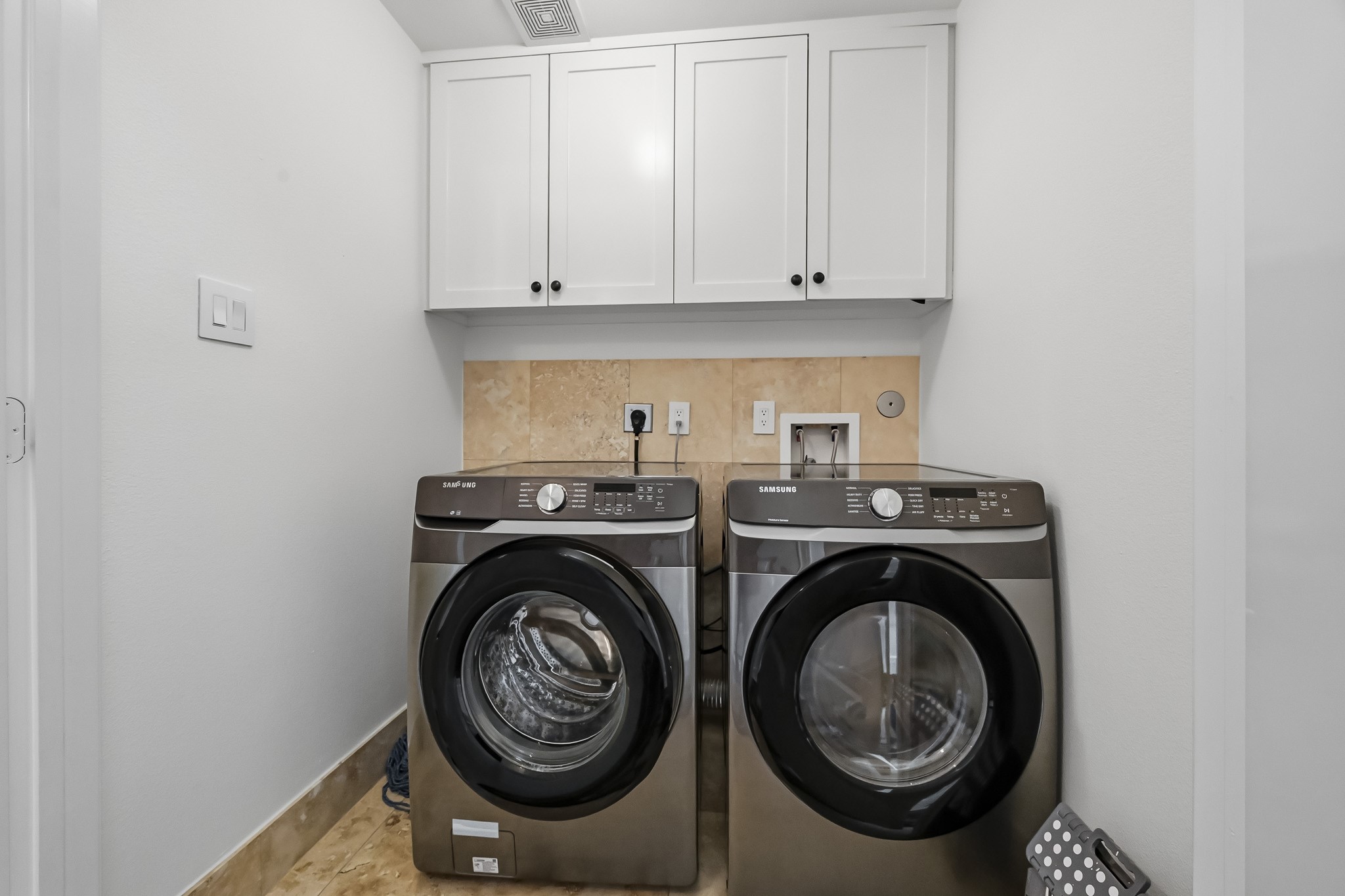 Modern laundry area featuring sleek front-loading washer and dryer units, complemented by overhead cabinetry for ample storage.