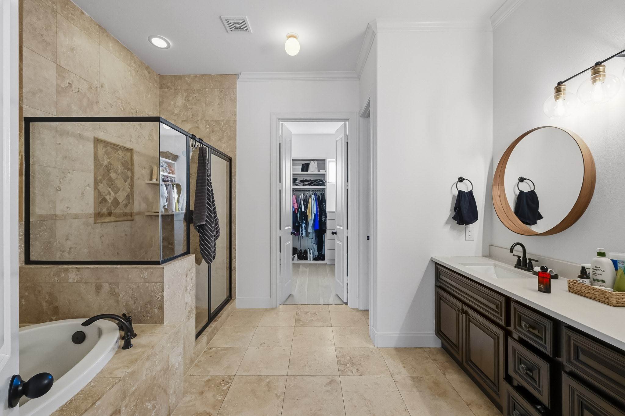 Elegant bathroom featuring a spacious walk-in shower with glass enclosure, luxurious soaking tub, and dual vanity with stylish lighting, leading to a roomy walk-in closet.